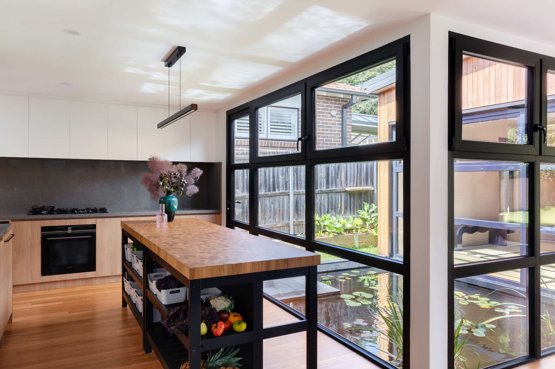 This Japanese-inspired kitchen has views of a tranquil reflection pond, blending natural textures with clean, modern lines. Black-framed windows flood the space with light, while the butcher-block island adds warmth and artisanal character.