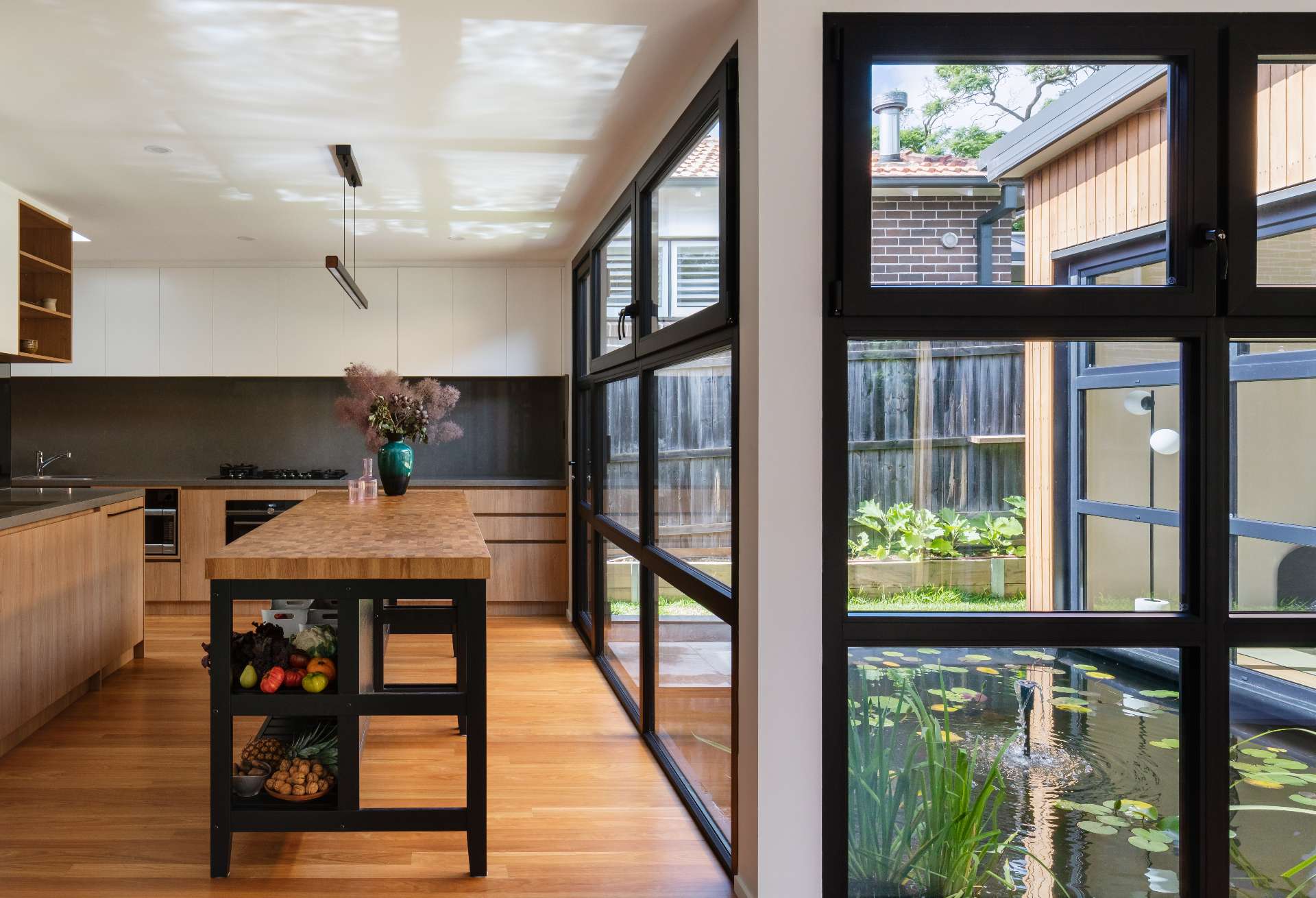 This Japanese-inspired kitchen has views of a tranquil reflection pond, blending natural textures with clean, modern lines. Black-framed windows flood the space with light, while the butcher-block island adds warmth and artisanal character.