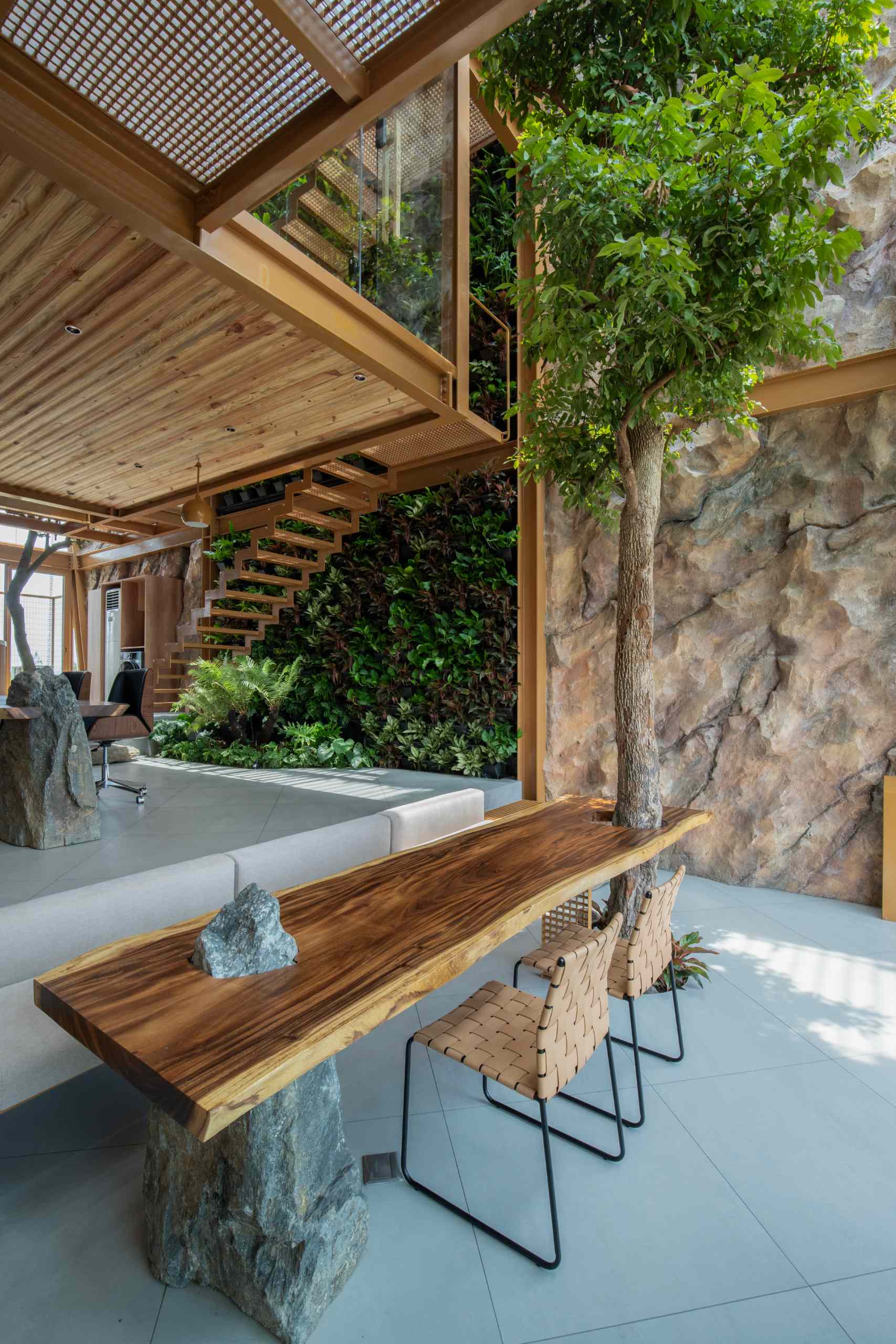 A full-grown tree rises through a custom wood slab table, blending nature with furniture in a playful, grounded way. The table’s rich grain and organic edge add warmth, while a stone base brings an earthy, solid touch to the space.