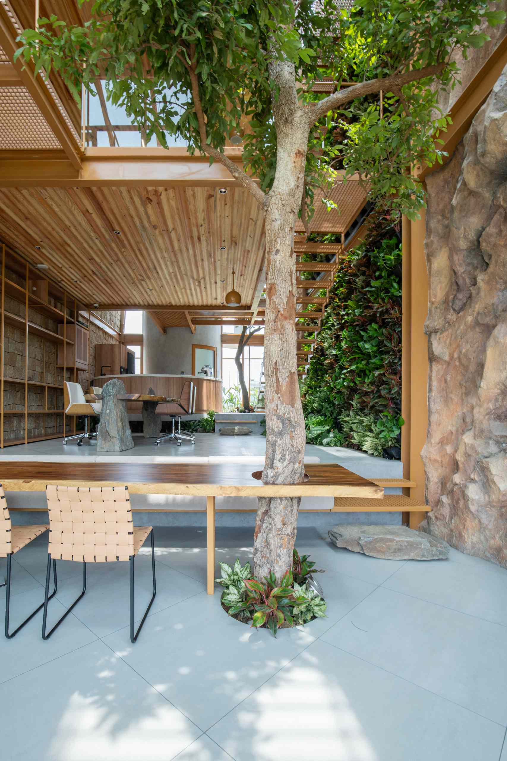 A full-grown tree rises through a custom wood slab table, blending nature with furniture in a playful, grounded way. The table’s rich grain and organic edge add warmth, while a stone base brings an earthy, solid touch to the space.