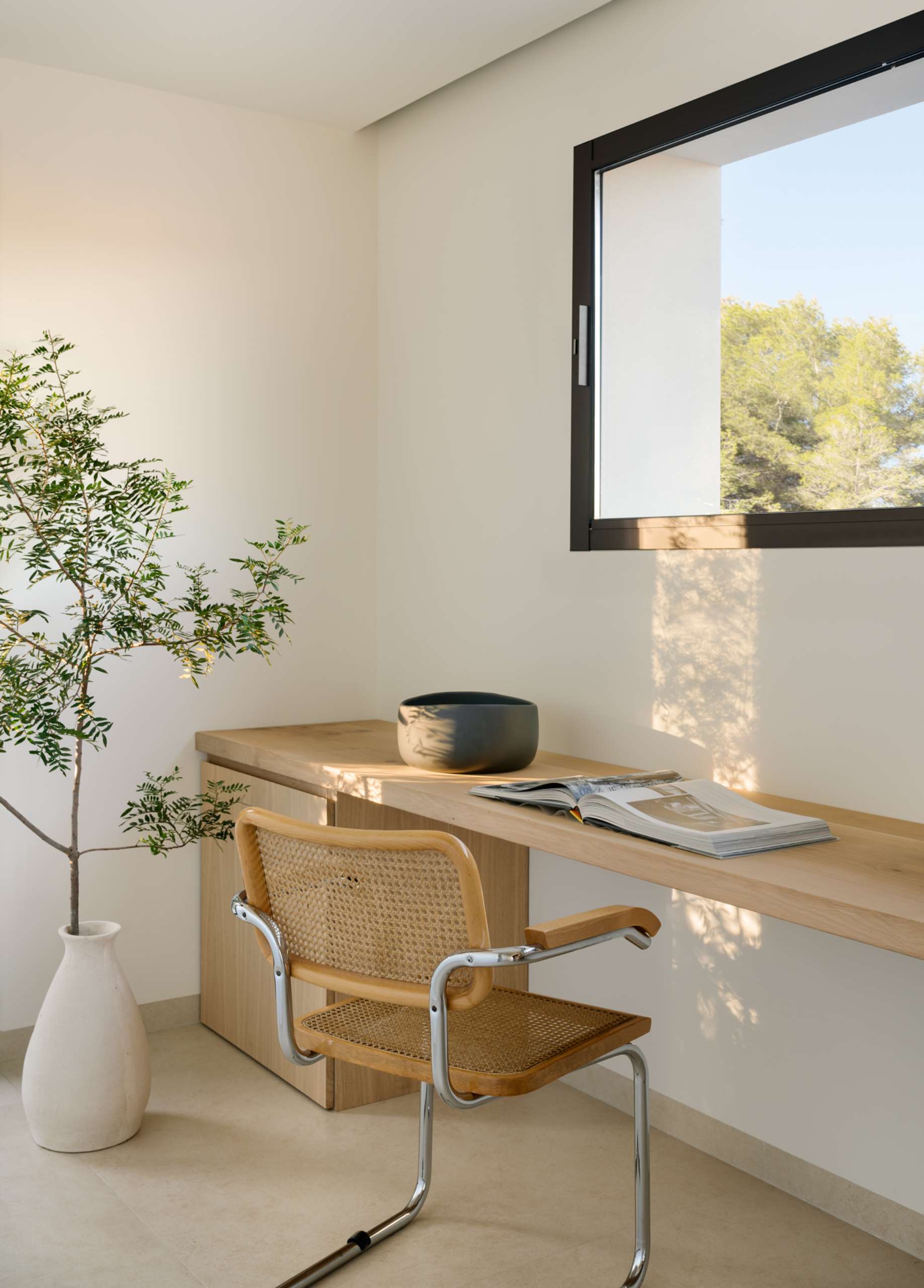 A serene home office designed for focus without rigidity. Natural light bathes the space, highlighting the clean lines of wood desk setup for two. Woven chairs, a leafy plant, and minimal decor reinforce the balance between functionality and calm.
