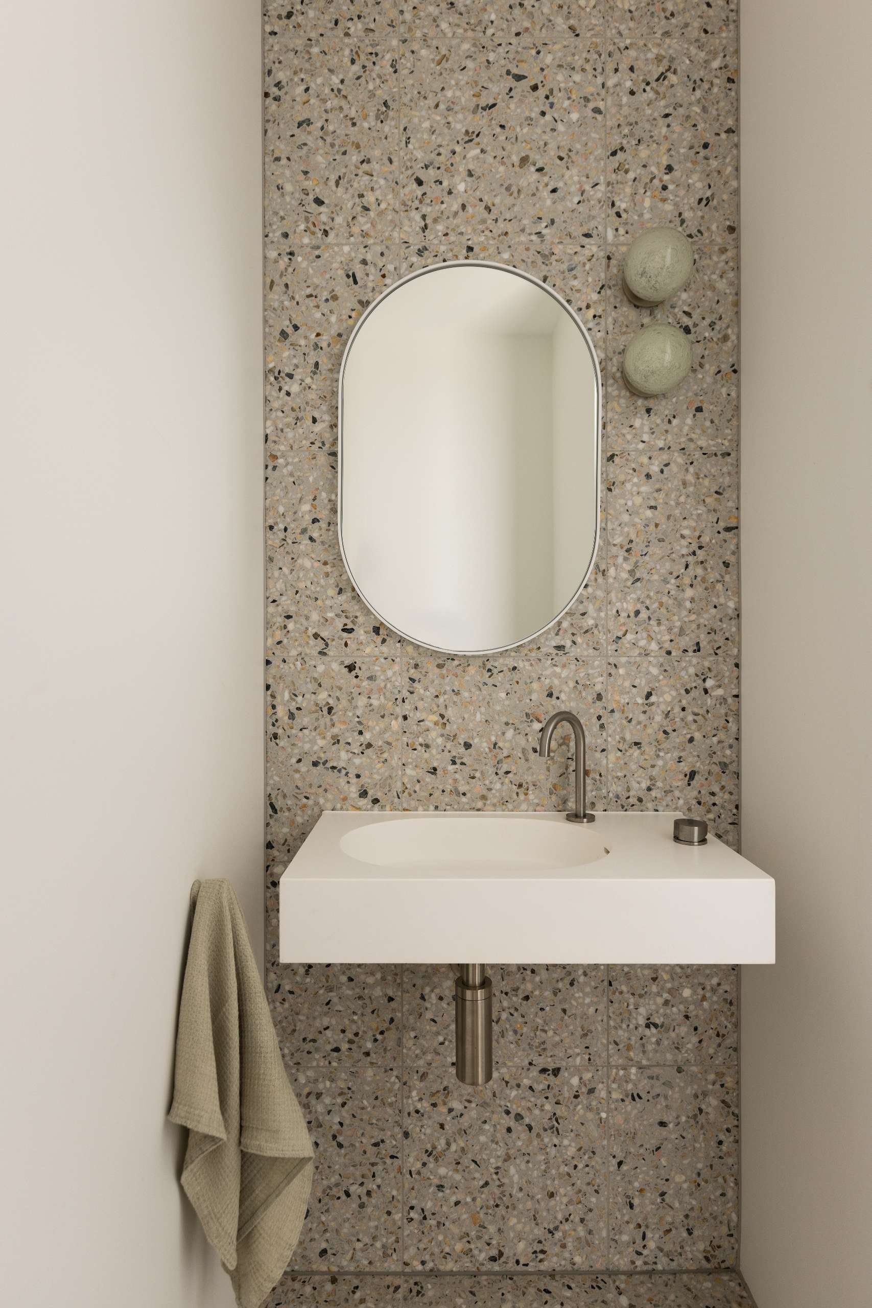 This powder room pairs a terrazzo-tiled wall with a sleek floating vanity and rounded mirror. Soft lighting and a muted palette create a calm, refined feel in a compact space.