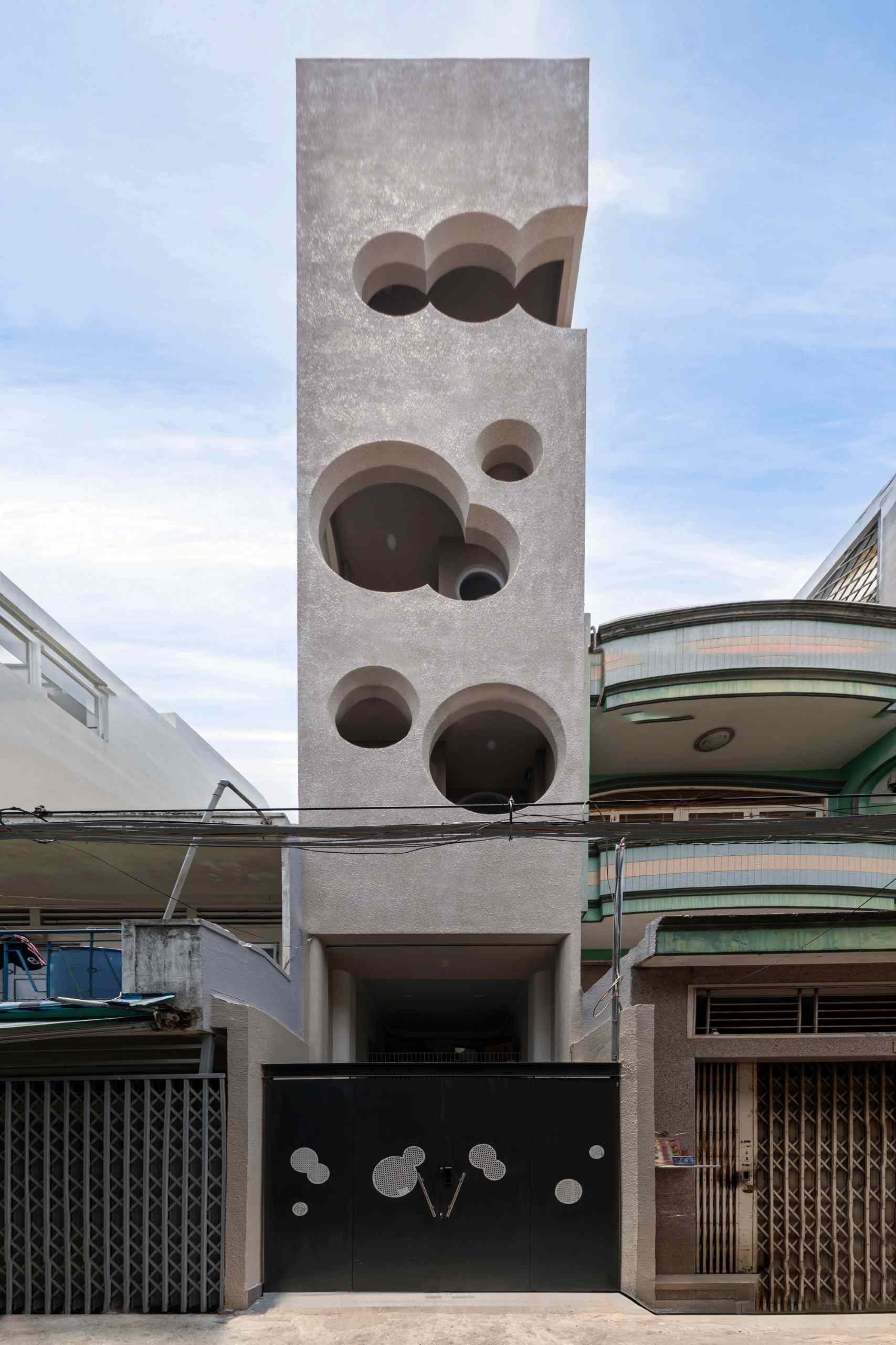 A modern apartment building fills a narrow lot and features cloud-shaped openings.