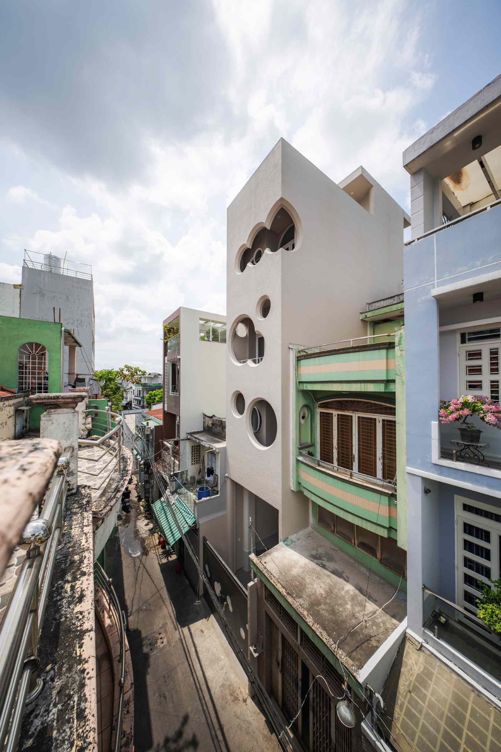 A modern apartment building fills a narrow lot and features cloud-shaped openings.