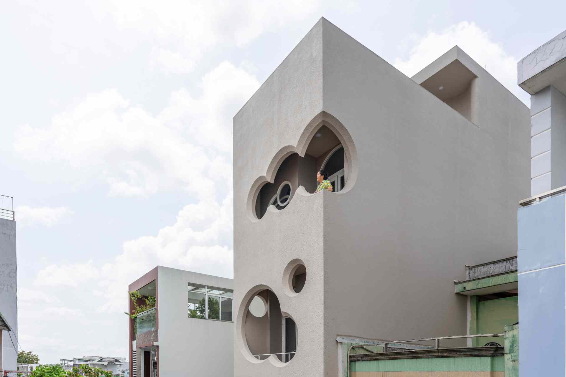 A modern apartment building fills a narrow lot and features cloud-shaped openings.