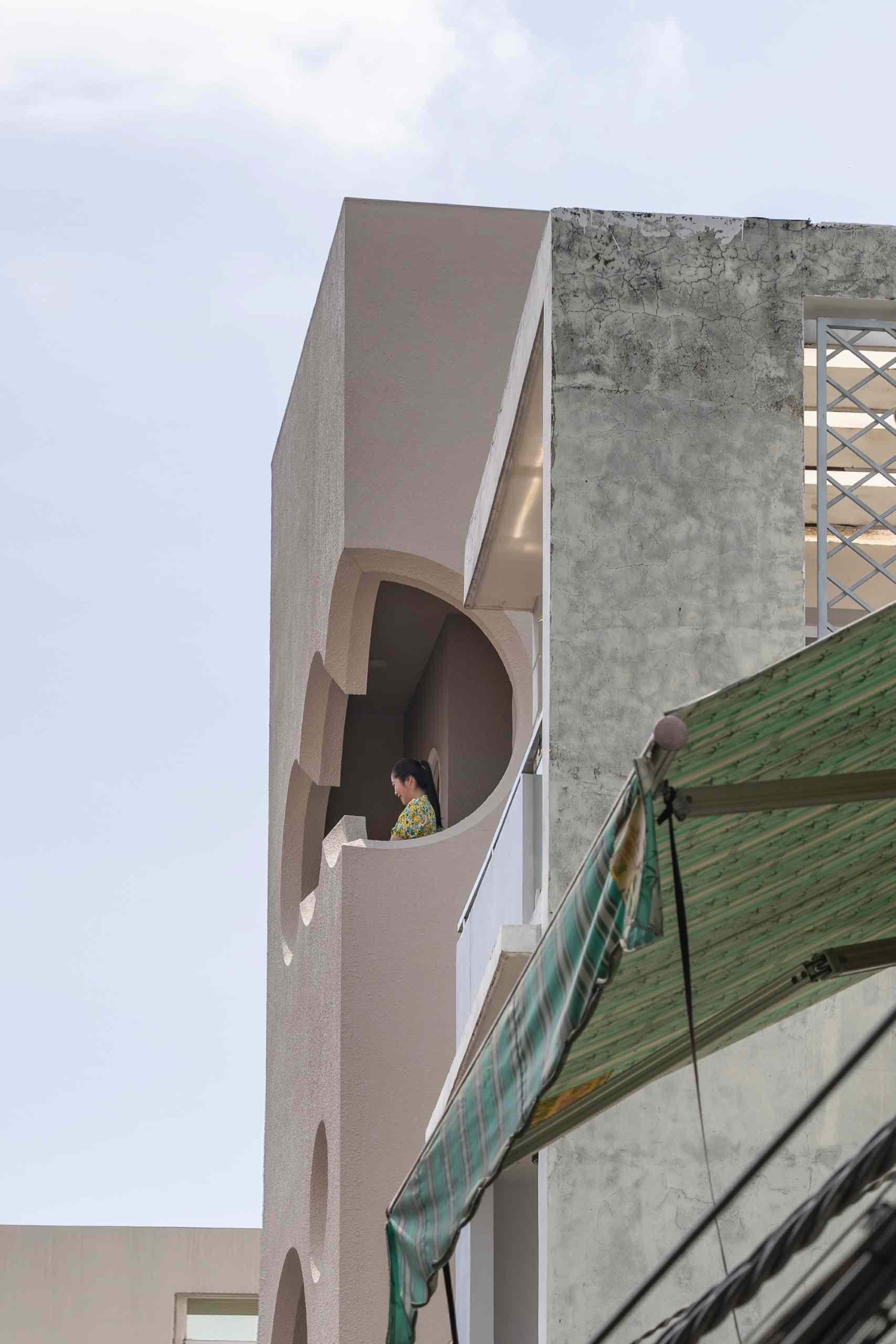 A modern apartment building fills a narrow lot and features cloud-shaped openings.