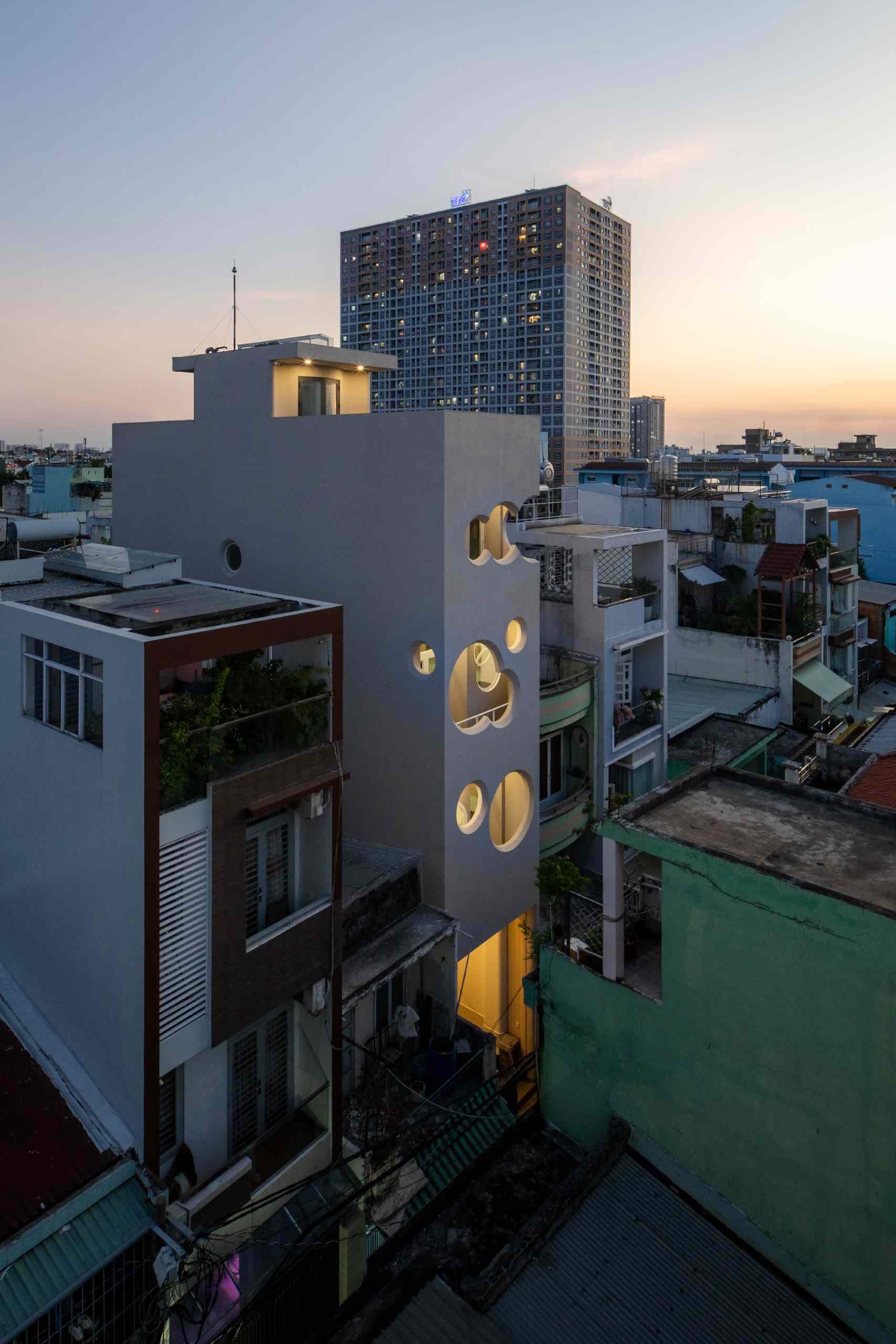 A modern apartment building fills a narrow lot and features cloud-shaped openings.