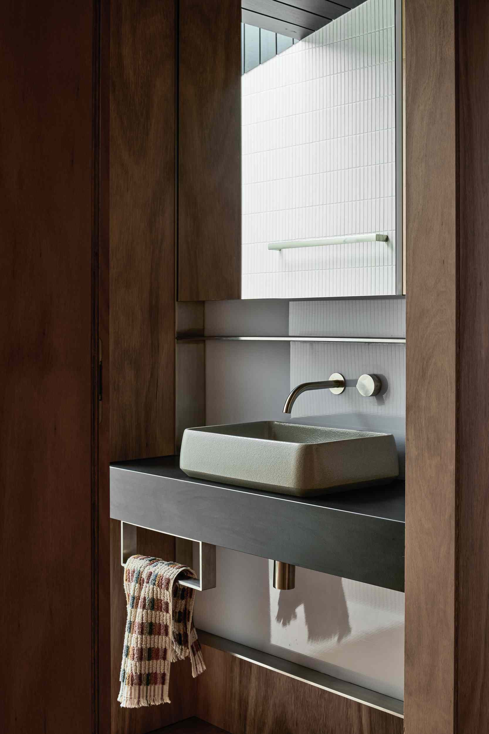In this bathroom, there's a dark countertop and soft sage basin. Warm timber joinery and brushed metal fixtures complete the clean, contemporary look