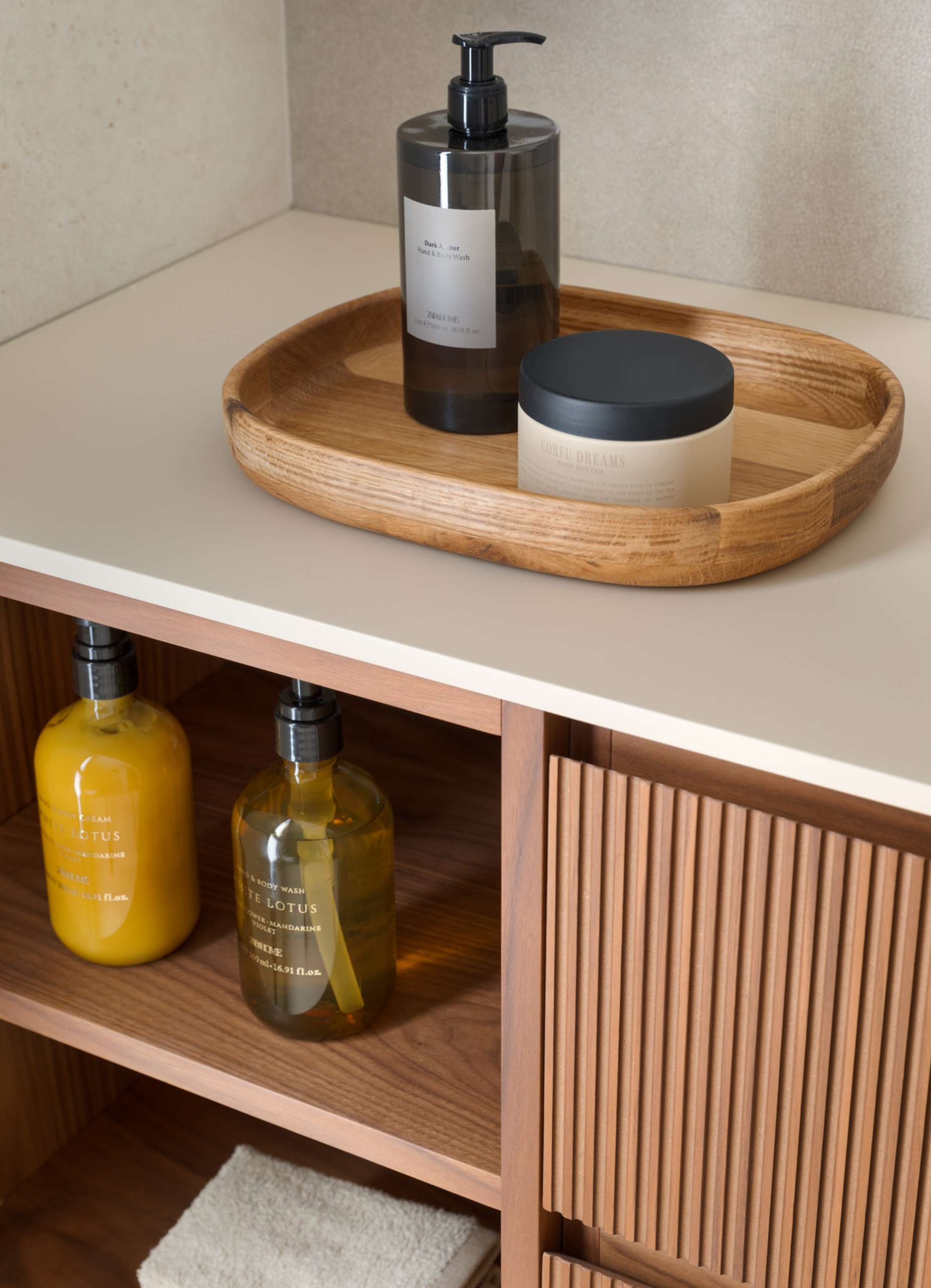 Clean lines and warm materials define the bathroom’s quiet elegance. A fluted timber vanity adds tactile interest beneath a wide mirror, while stone-look tiles and twin basins enhance the sense of space. Bronze fixtures introduce just a hint of glow, elevating the room without overpowering its simplicity.