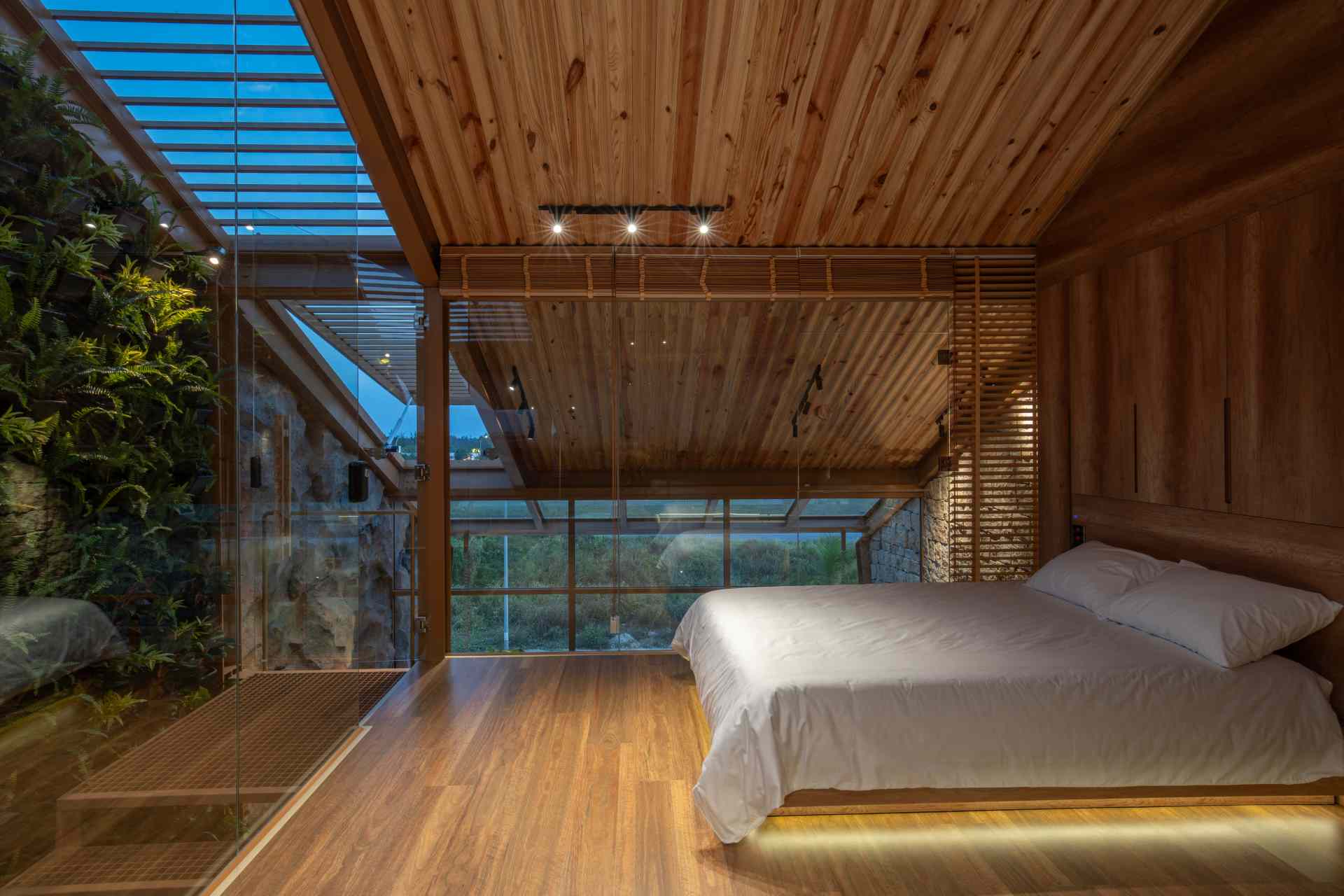 Bedroom with a pitched wooden ceiling, custom built-in cabinetry, and beds positioned between two walls of floor-to-ceiling glass that flood the space with natural light.