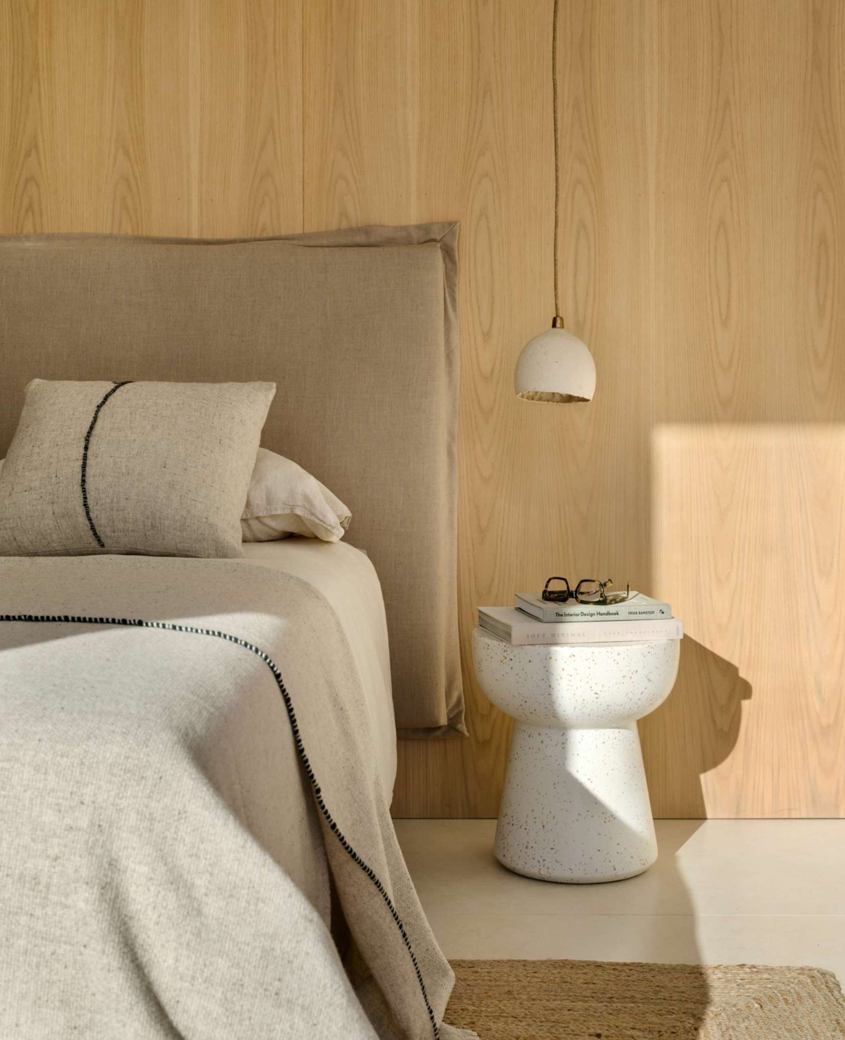 The design of this bedroom is an exercise in restful restraint. Sunlight filters through sliding doors that open onto a balcony surrounded by lush greenery, while soft linen bedding, natural textures, and minimal styling keep the mood grounded. A timber feature wall adds quiet warmth, and sculptural accents, from side tables to abstract art, offer subtle personality within the calm palette. It’s a room designed for retreat, where every element supports peace.