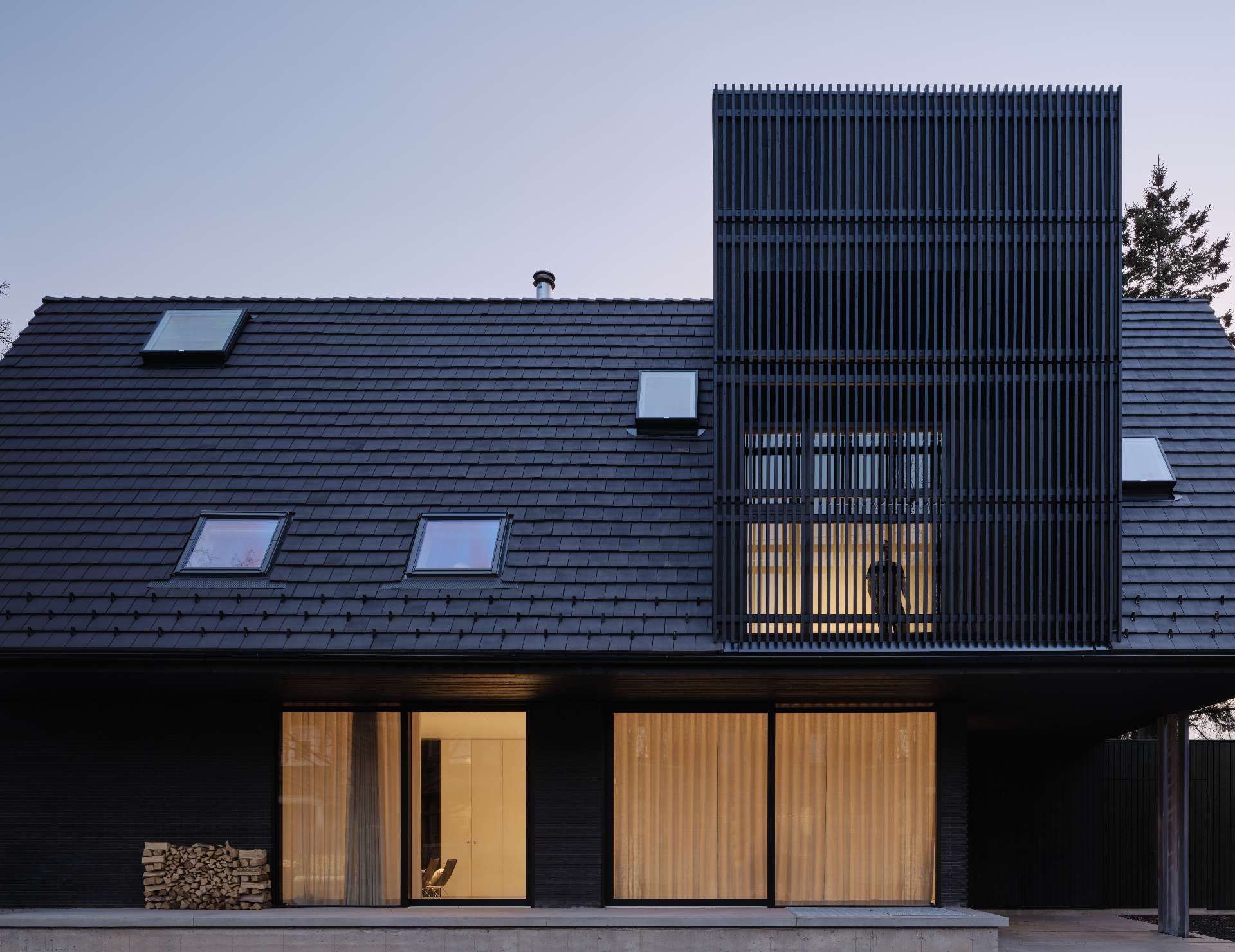 The palette of this modern home with a steep pitched roof, includes terracotta roof shingles, hand pressed brick, vertical hand brushed wood siding, powder-coated aluminum details, and raw galvanized steel.