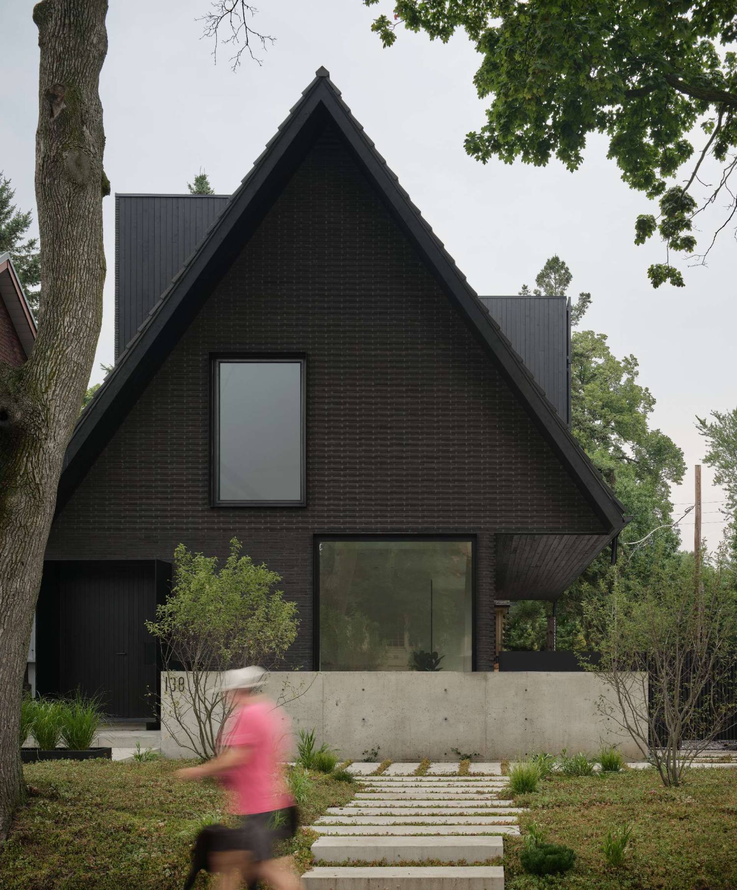 The palette of this modern home with a steep pitched roof, includes terracotta roof shingles, hand pressed brick, vertical hand brushed wood siding, powder-coated aluminum details, and raw galvanized steel.
