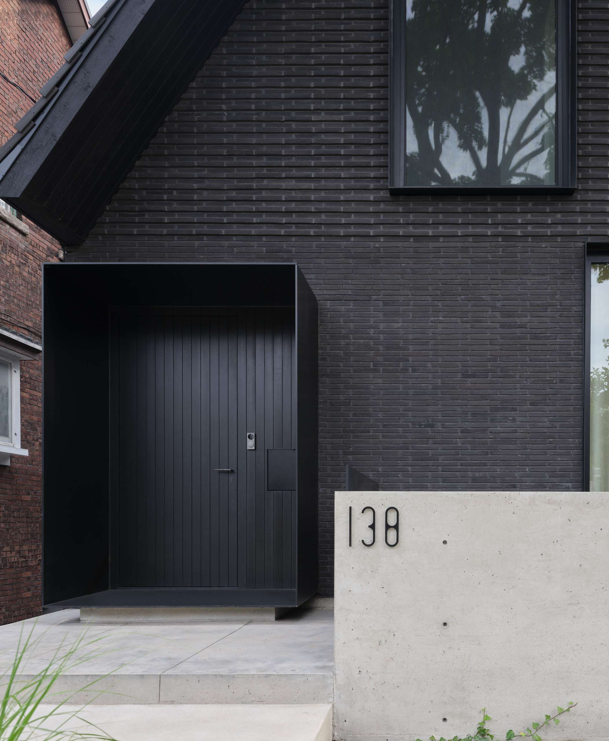 The palette of this modern home with a steep pitched roof, includes terracotta roof shingles, hand pressed brick, vertical hand brushed wood siding, powder-coated aluminum details, and raw galvanized steel.