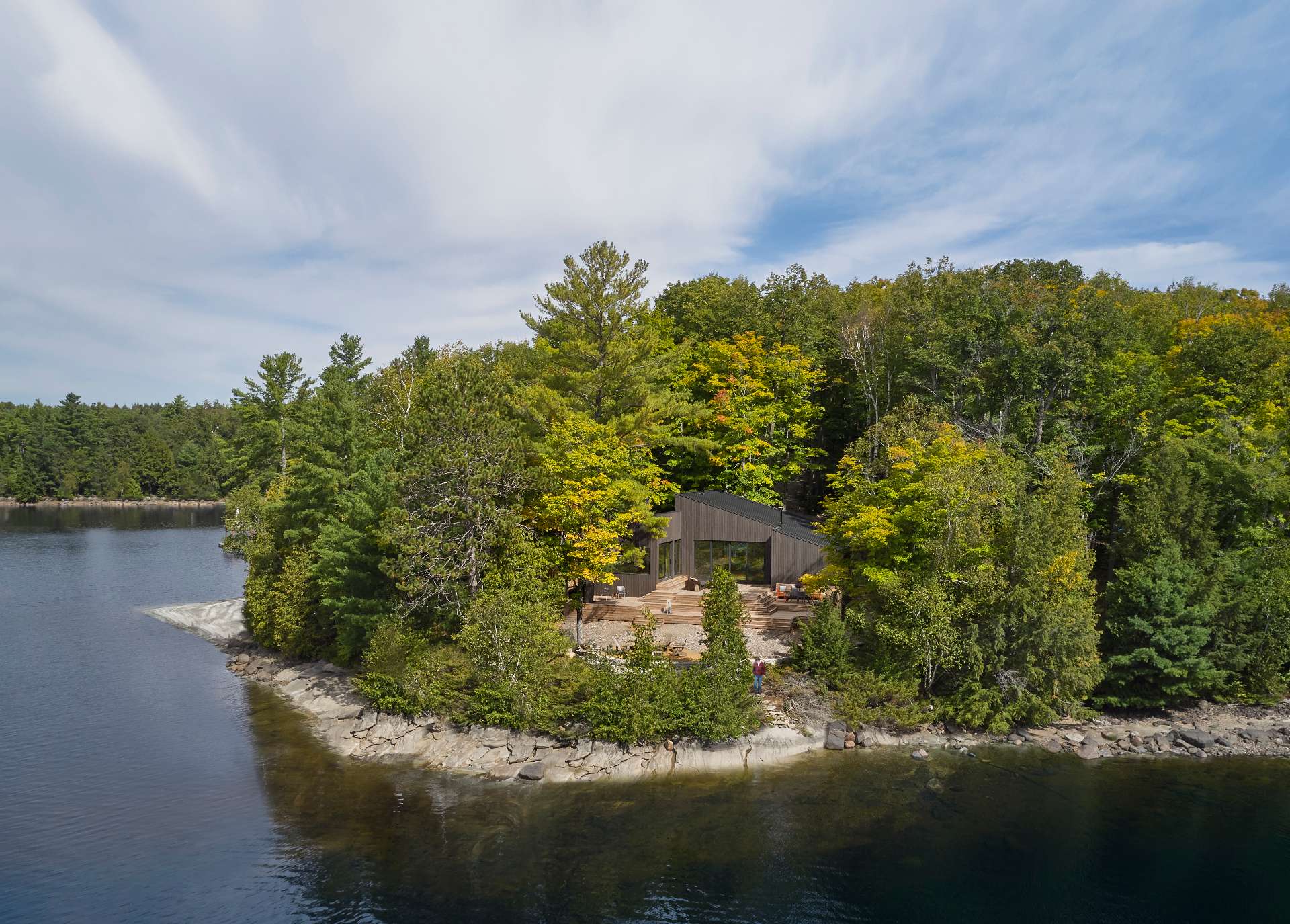 A modern one-storey cottage has three distinct volumes with integrated steep rooflines, and a large wood deck with multiple levels.