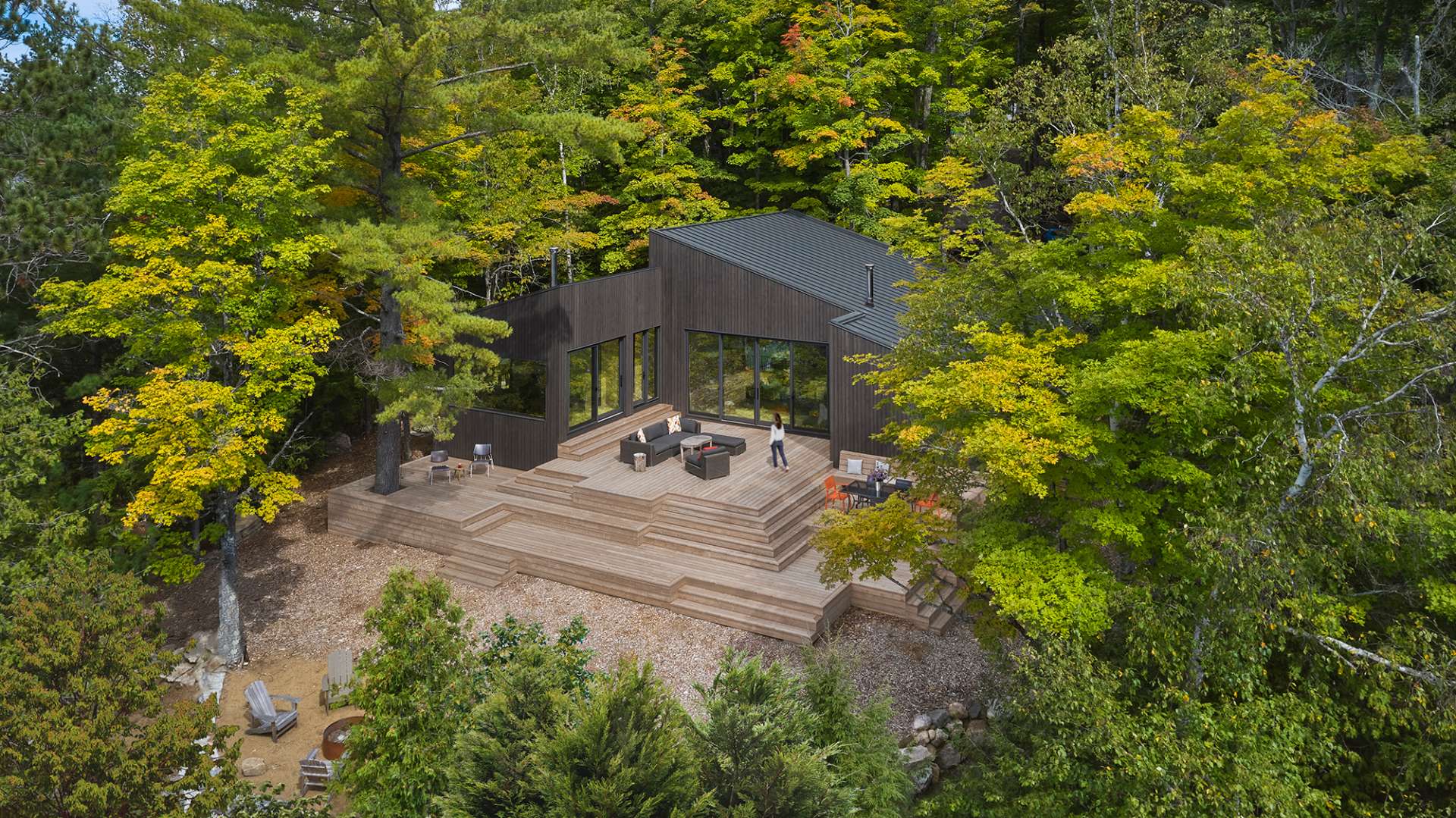 A modern one-storey cottage has three distinct volumes with integrated steep rooflines, and a large wood deck with multiple levels.