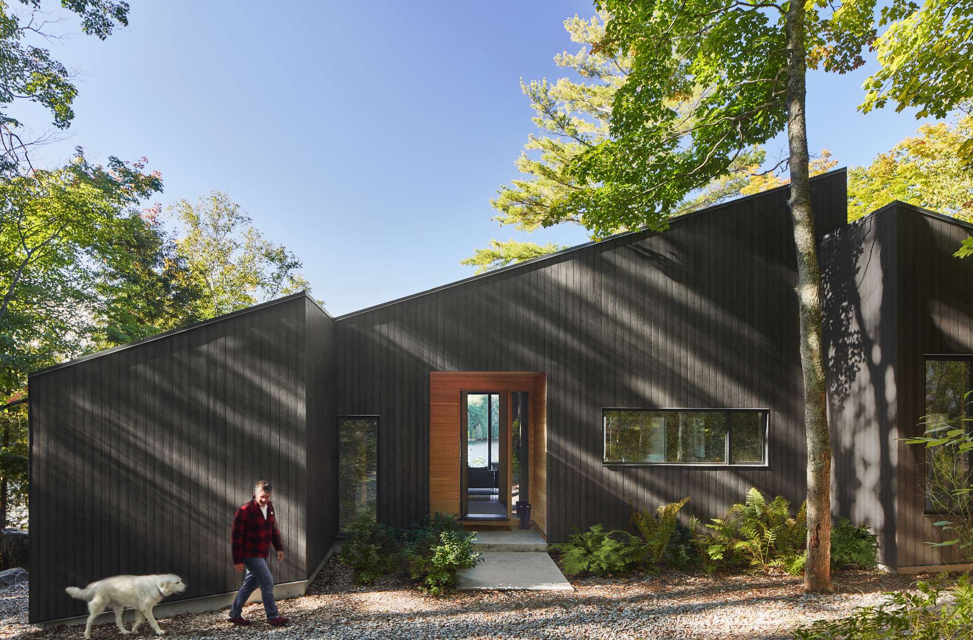 The entry porch of this modern cottage is carved out of the main volume and lined with warm red cedar, contrasting the darkened wood siding.