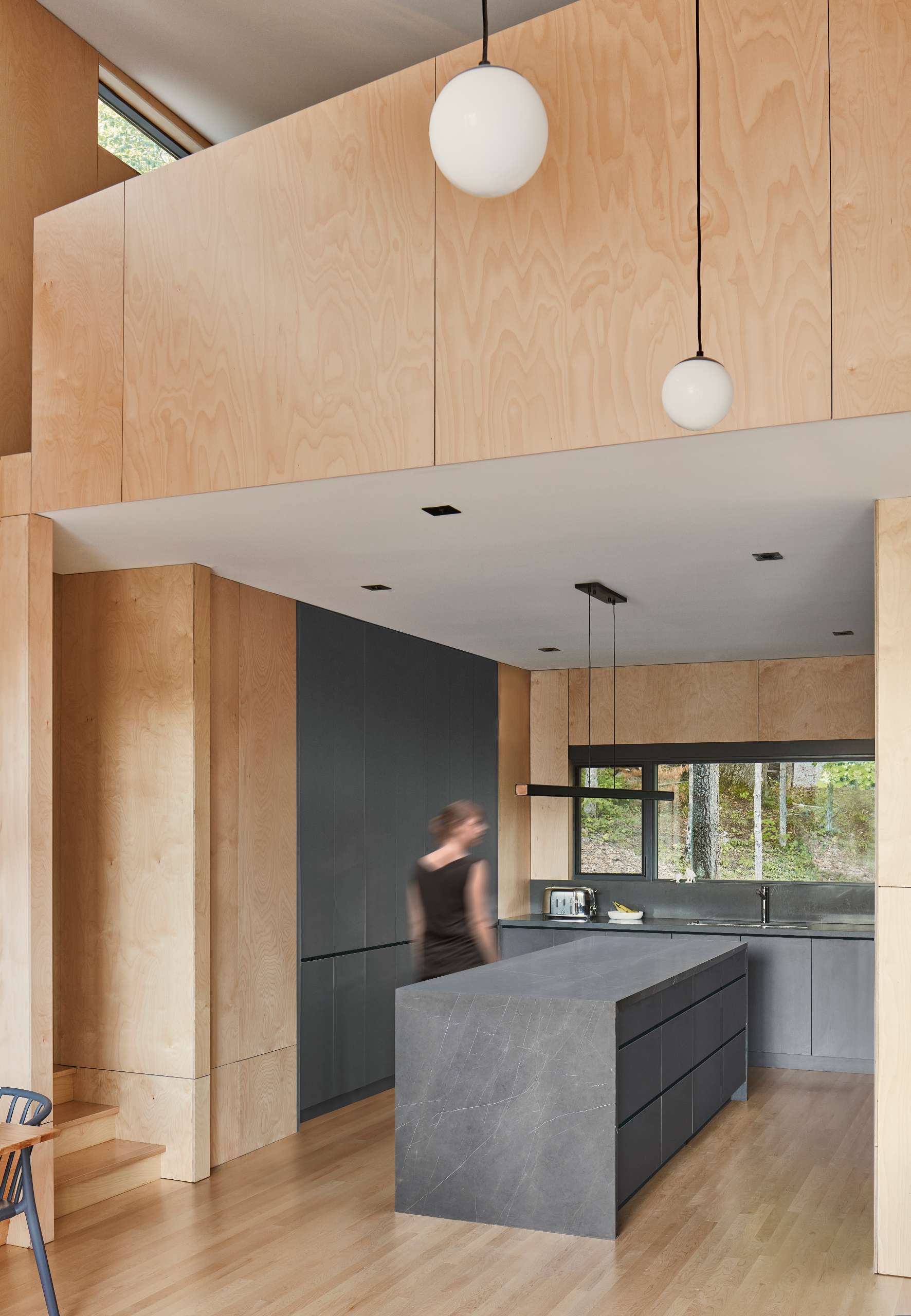 This modern kitchen contrasts the warm hues of maple plywood with cool greys. It features Greystone counters, charcoal cabinetry, and a waterfall island.