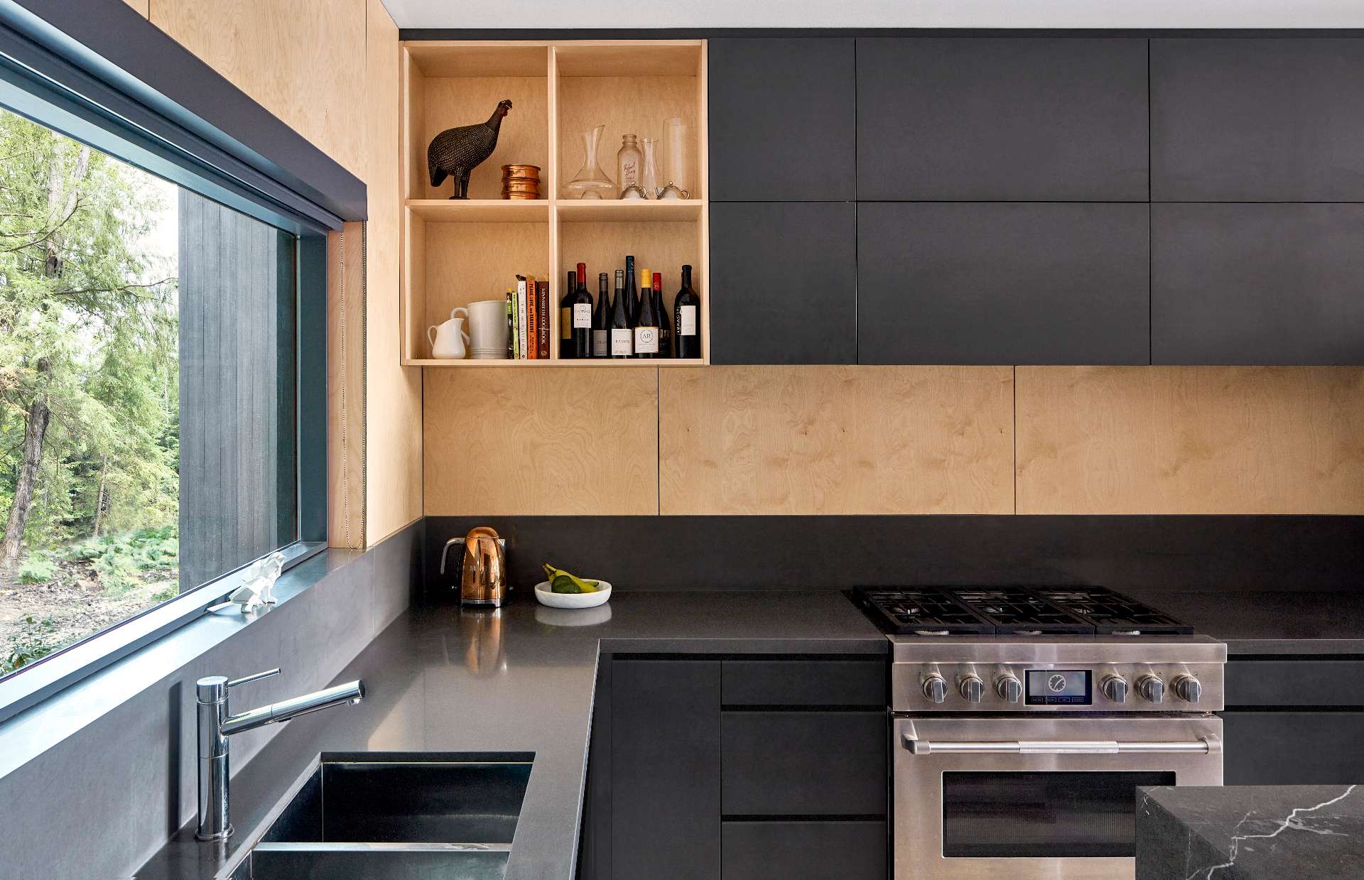 This modern kitchen contrasts the warm hues of maple plywood with cool greys. It features Greystone counters, charcoal cabinetry, and a waterfall island.