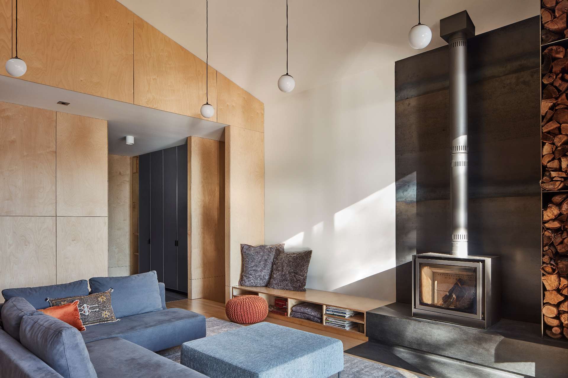 In the living room, a freestanding Stuv wood-burning stove is set on a slate stone ledge, complemented by a custom steel firewood storage solution.