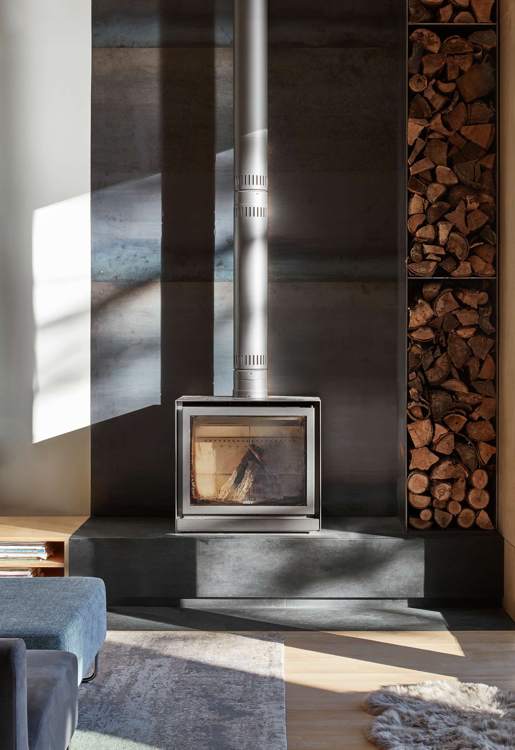 The cold-rolled steel behind the fireplace in this living room creates a striking contrast to the maple plywood-lined walls, adding visual interest and texture to the space.