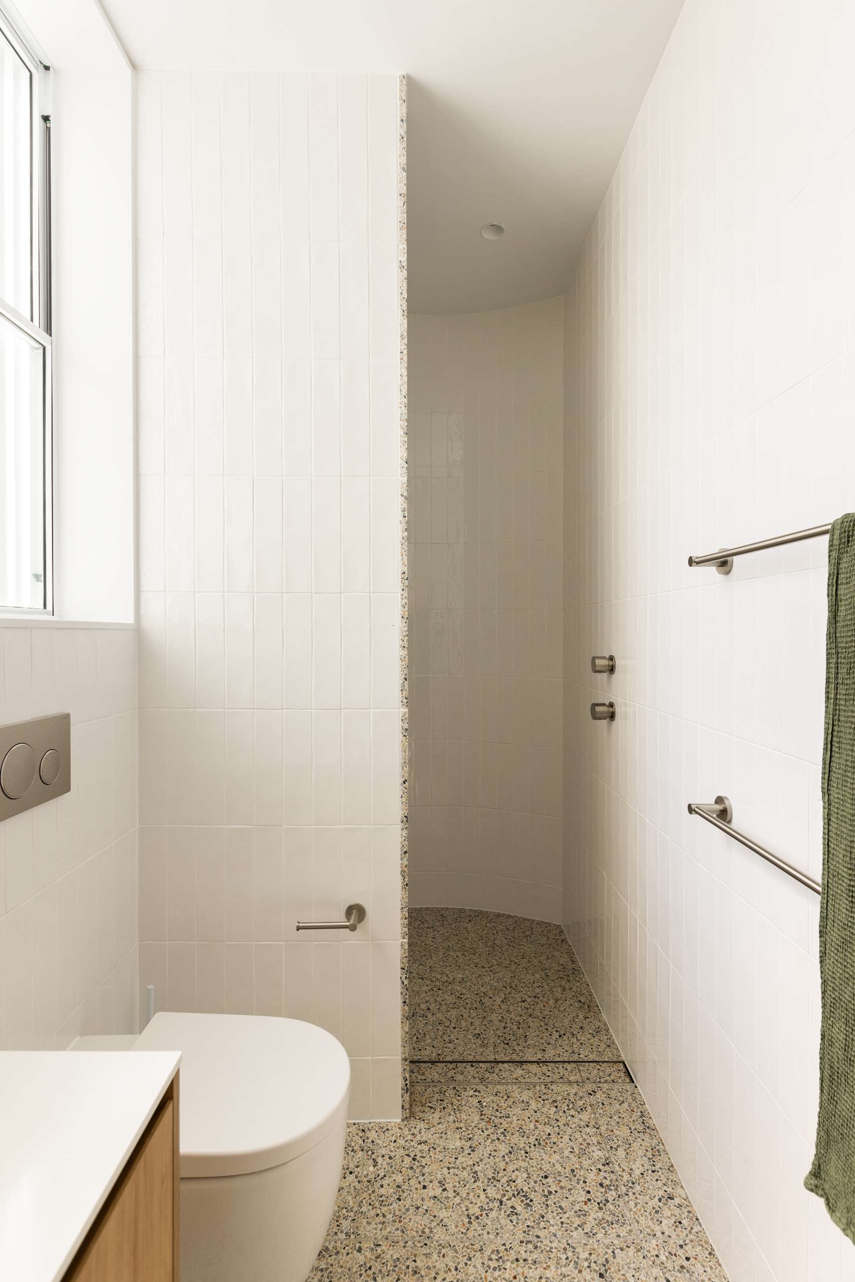 Soft curves and sculptural detail define this minimalist ensuite bathroom, where a terrazzo floor flows seamlessly into a curved walk-in shower. A soothing palette of white tile and natural textures completes the spa-like atmosphere.