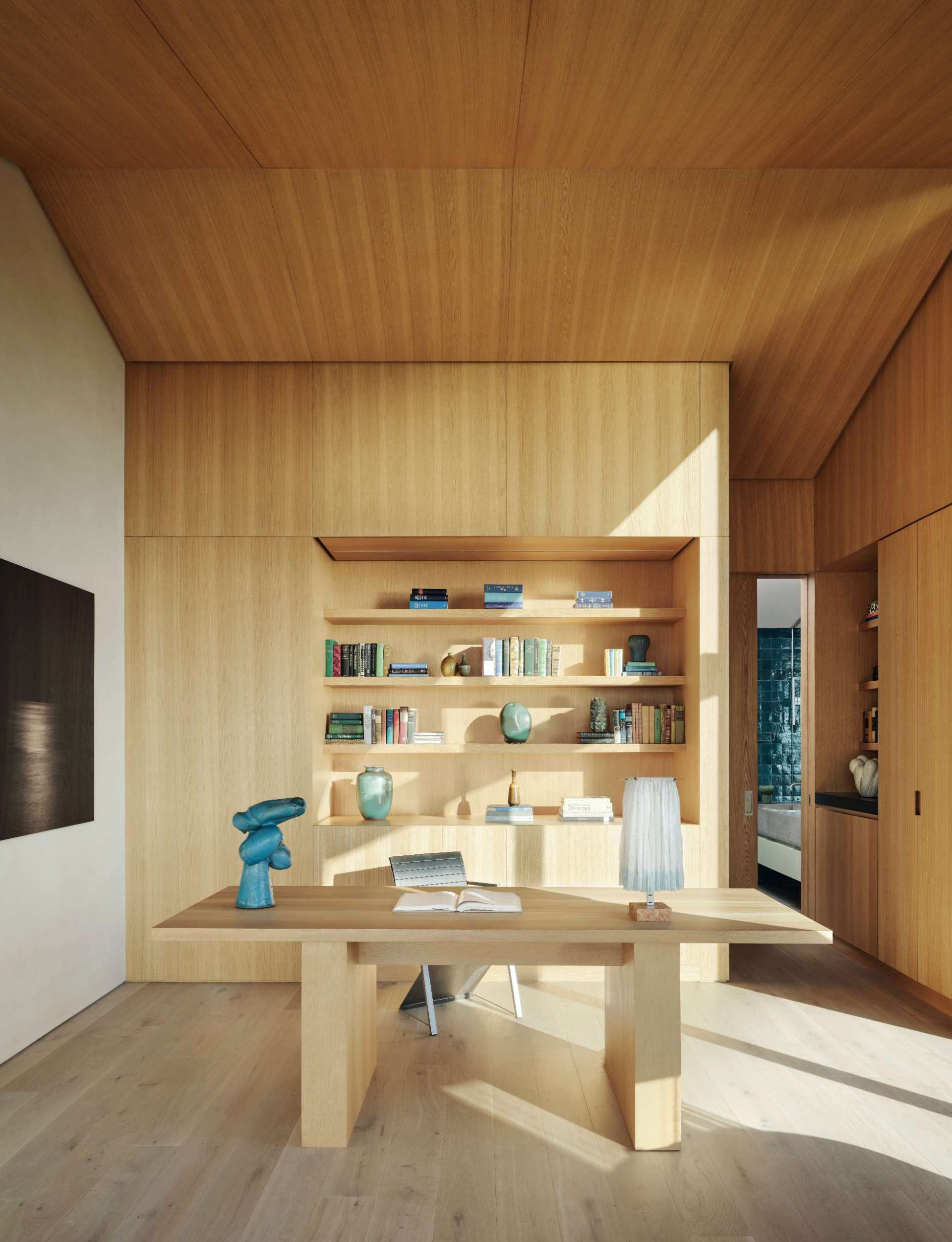A minimalist home office is enveloped in warm wood panelling, with integrated shelving displaying curated objects and books that bring a sense of character to the serene workspace.