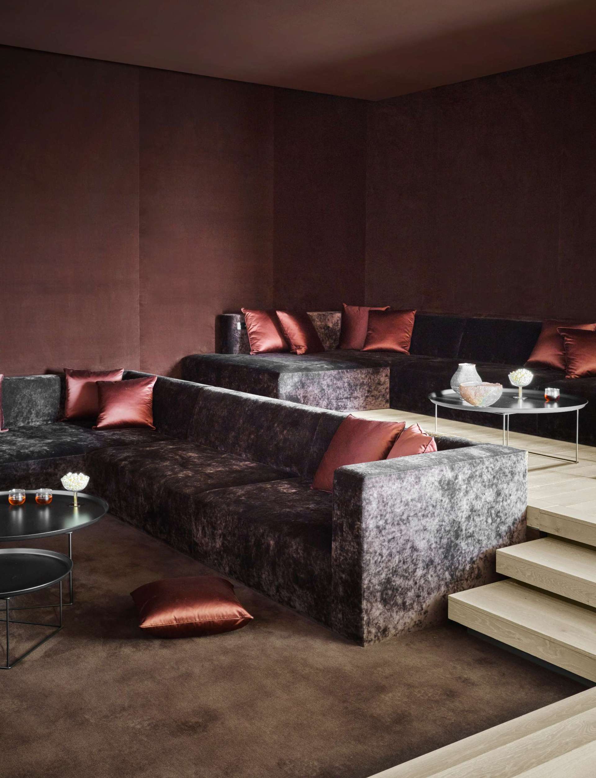 A sunken home theatre pairs luxurious sofas with rich brown tones and satin accents, creating a cocoon-like space for immersive viewing.