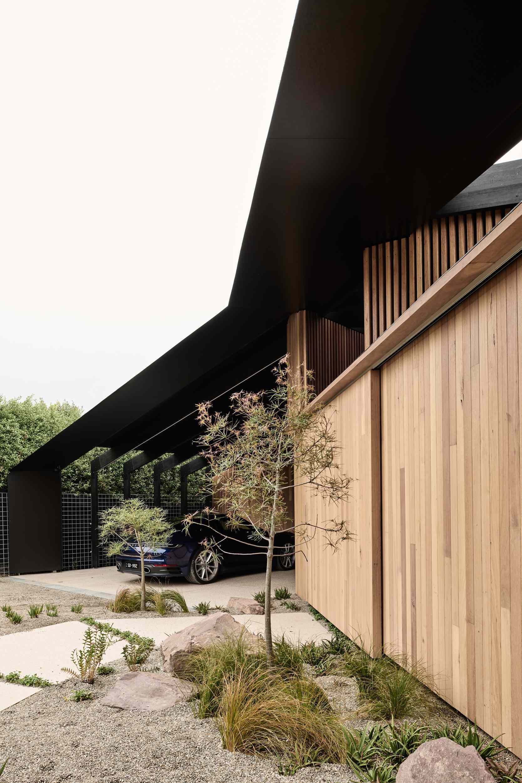 Under the deep eaves, this open carport is lined with black steel beams, adding a sculptural edge while providing practical shelter.
