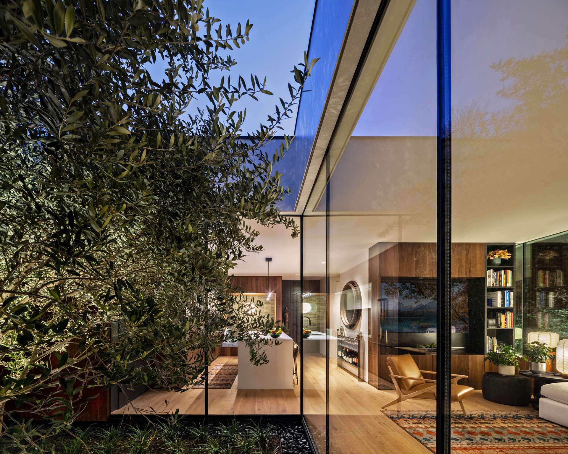 This serene courtyard anchors the home with a sculptural olive tree framed by floor-to-ceiling glass. Natural light floods the kitchen and living spaces while rusted steel cladding brings warmth and texture to the modern design.