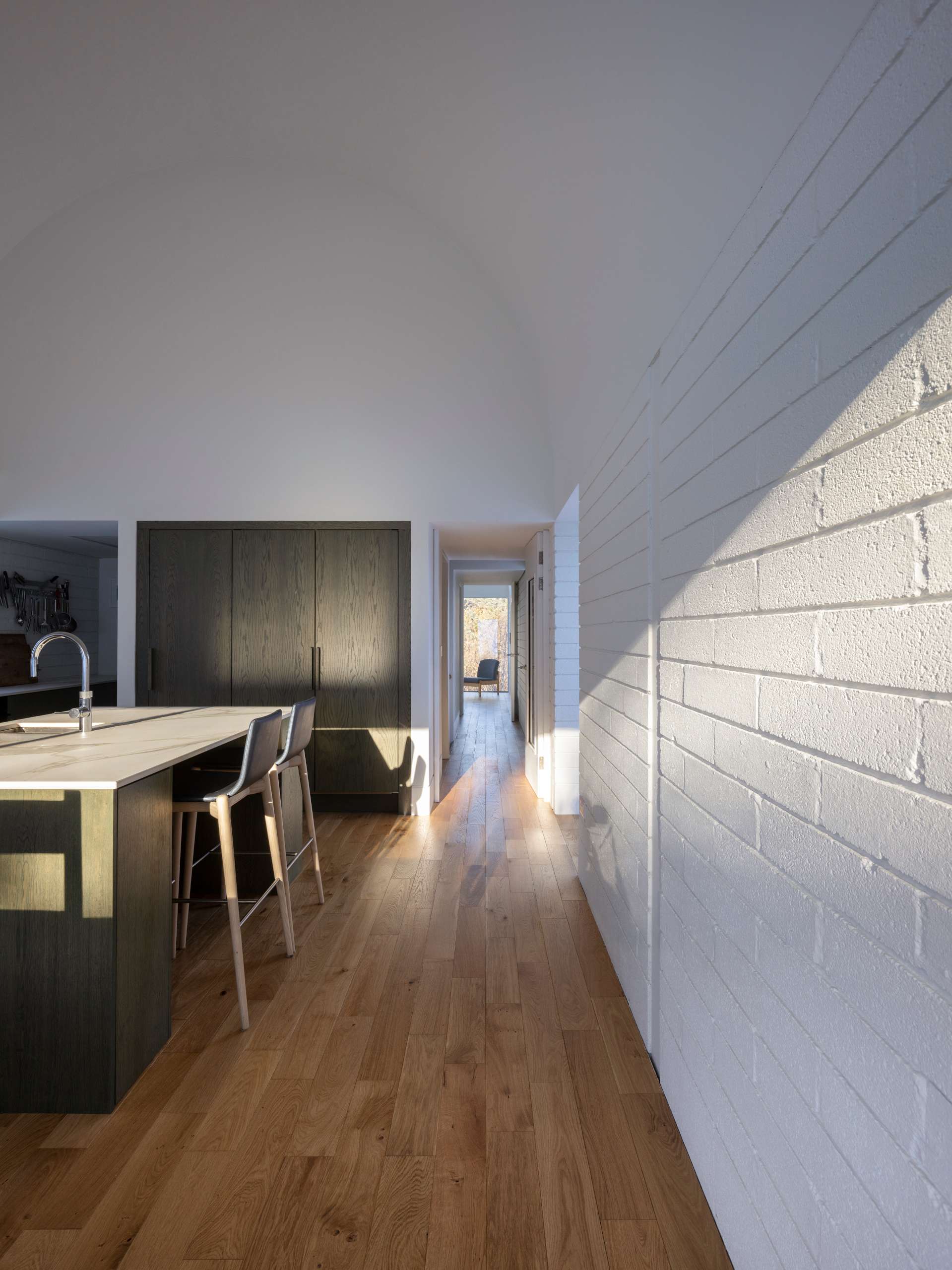 This serene kitchen pairs a vaulted ceiling with natural oak floors and marble countertops for a quietly luxurious feel. Floor-to-ceiling glass opens the space to snowy views, while warm wood tones and built-in seating create a calm, considered atmosphere that’s both functional and beautiful.