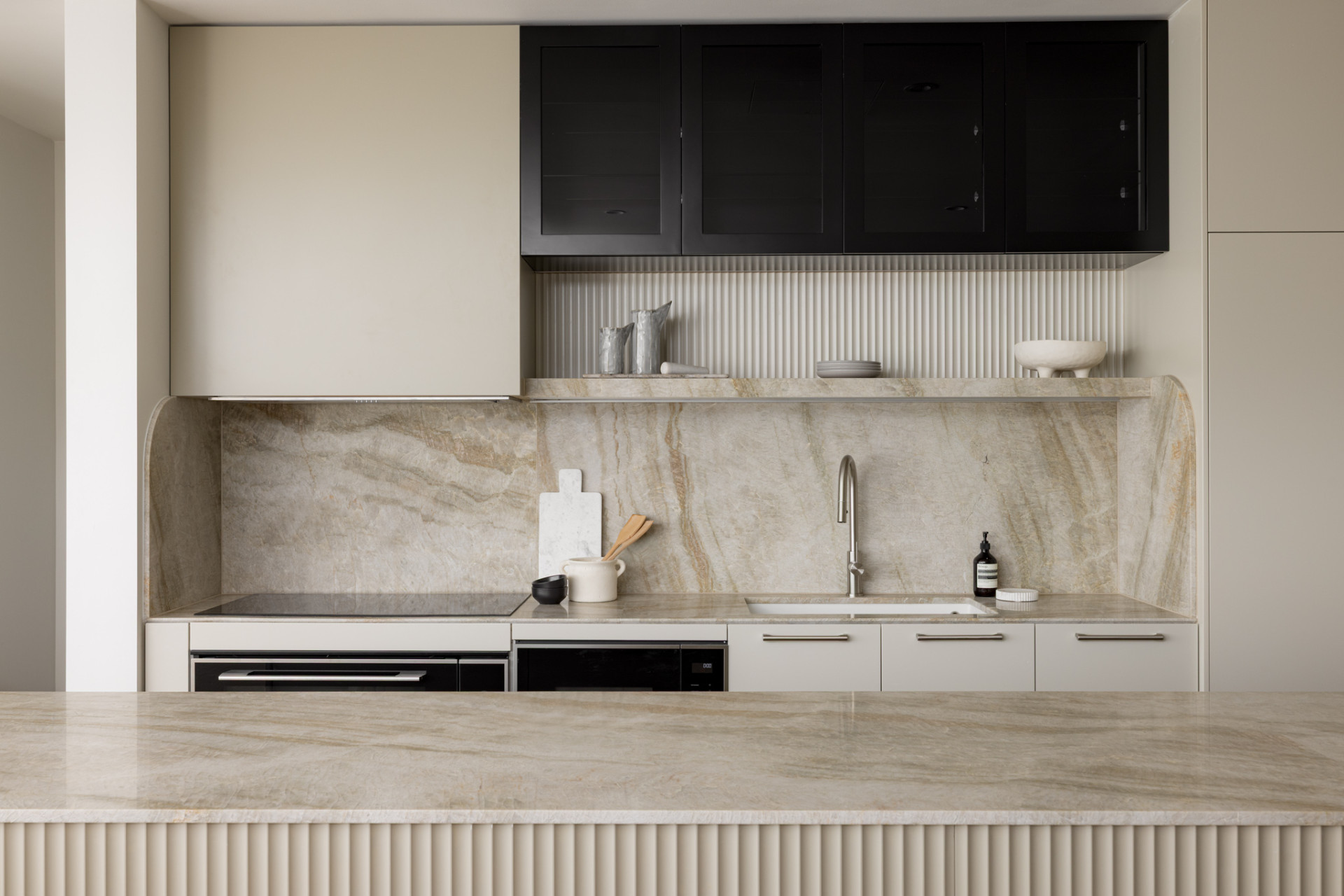 This modern kitchen has a large island with a fluted detail. The light and warm color tones chosen by the client to provide a tranquil and calming environment.