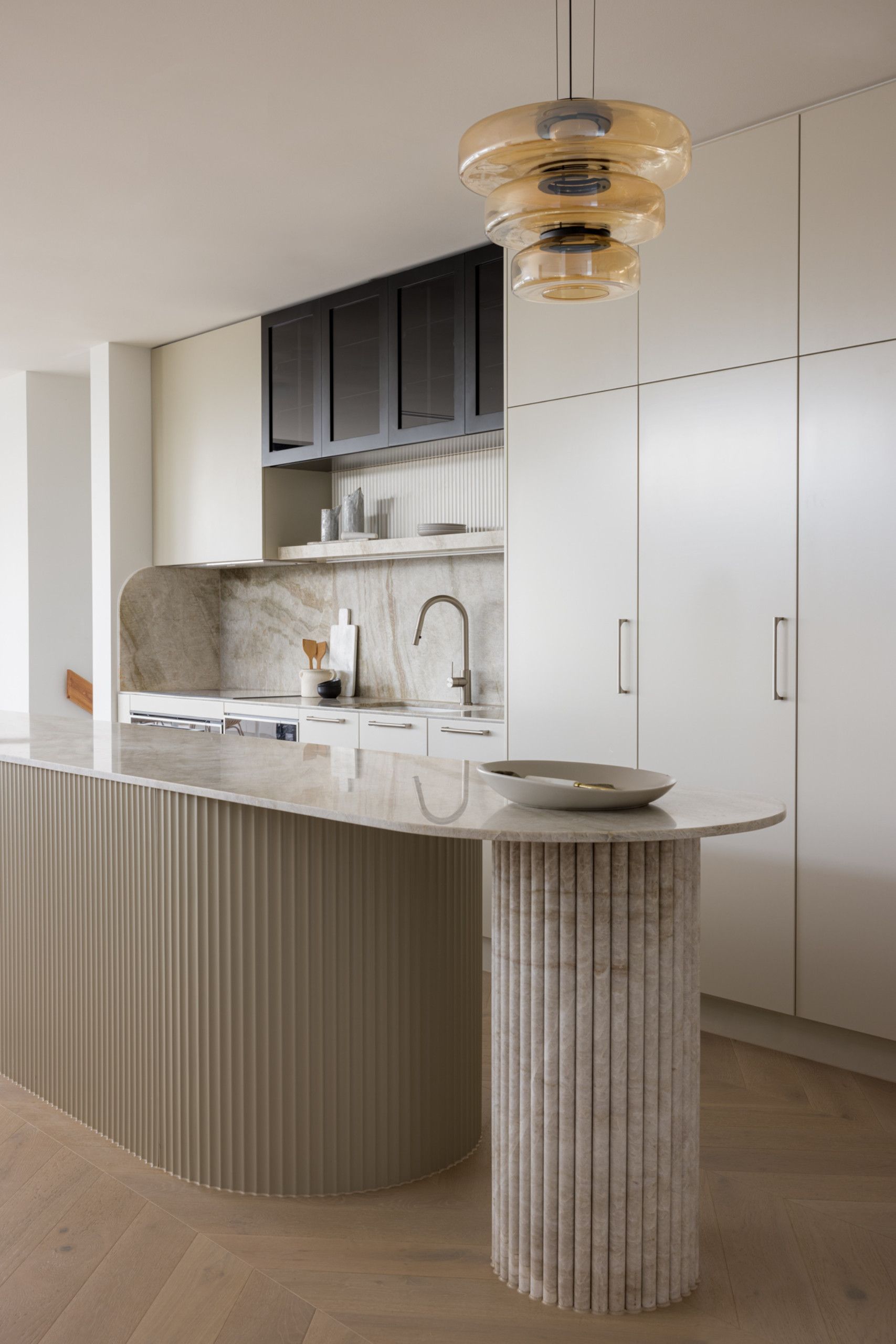 This modern kitchen has a large island with a fluted detail. The light and warm color tones chosen by the client to provide a tranquil and calming environment.