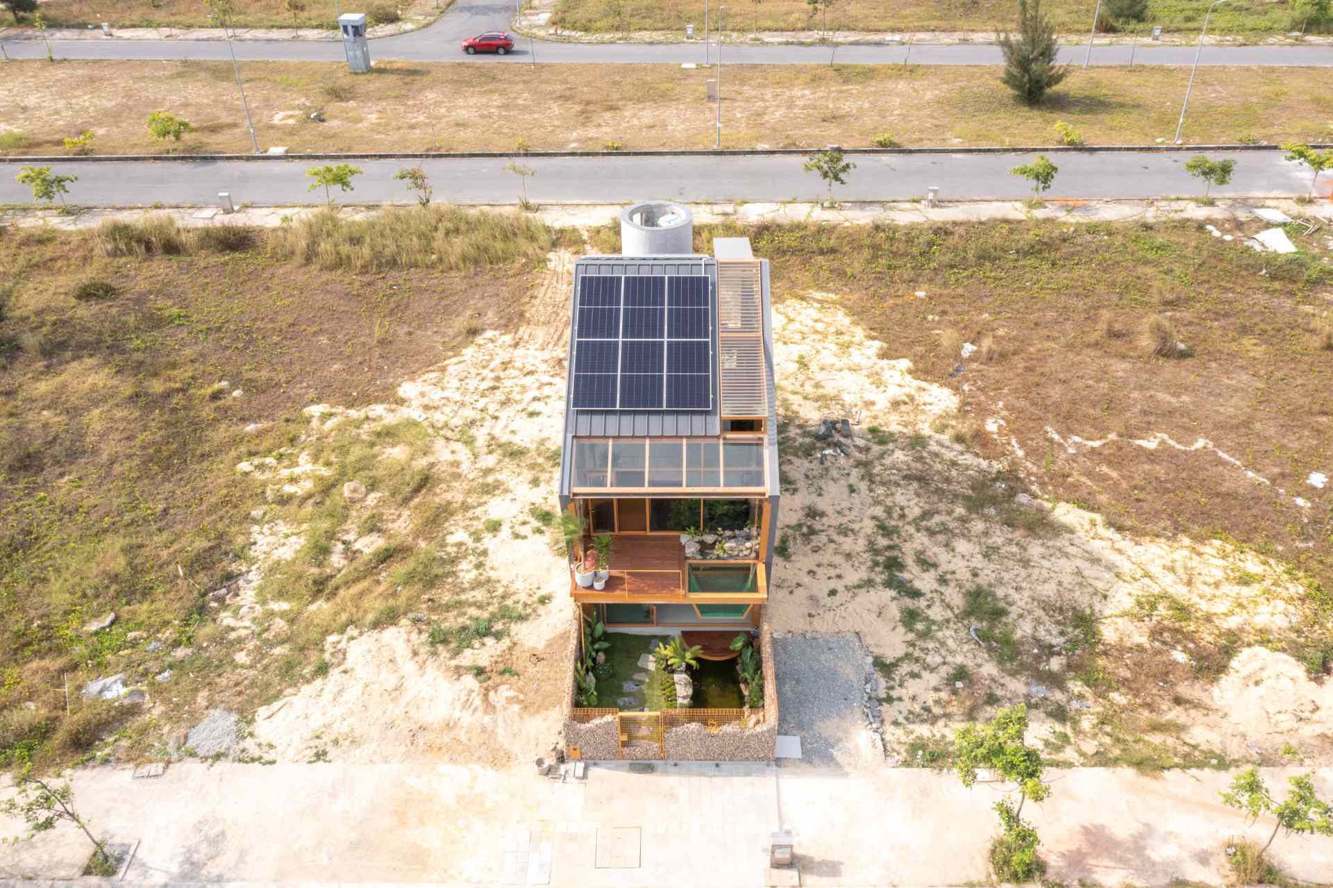 The exterior of this live-work building blends modern lines with natural materials, steel framing, warm wood, and wide glass panels. A glass box extending from the upper floor doubles as a water feature, while a stone-filled fence below adds texture and an earthy contrast.