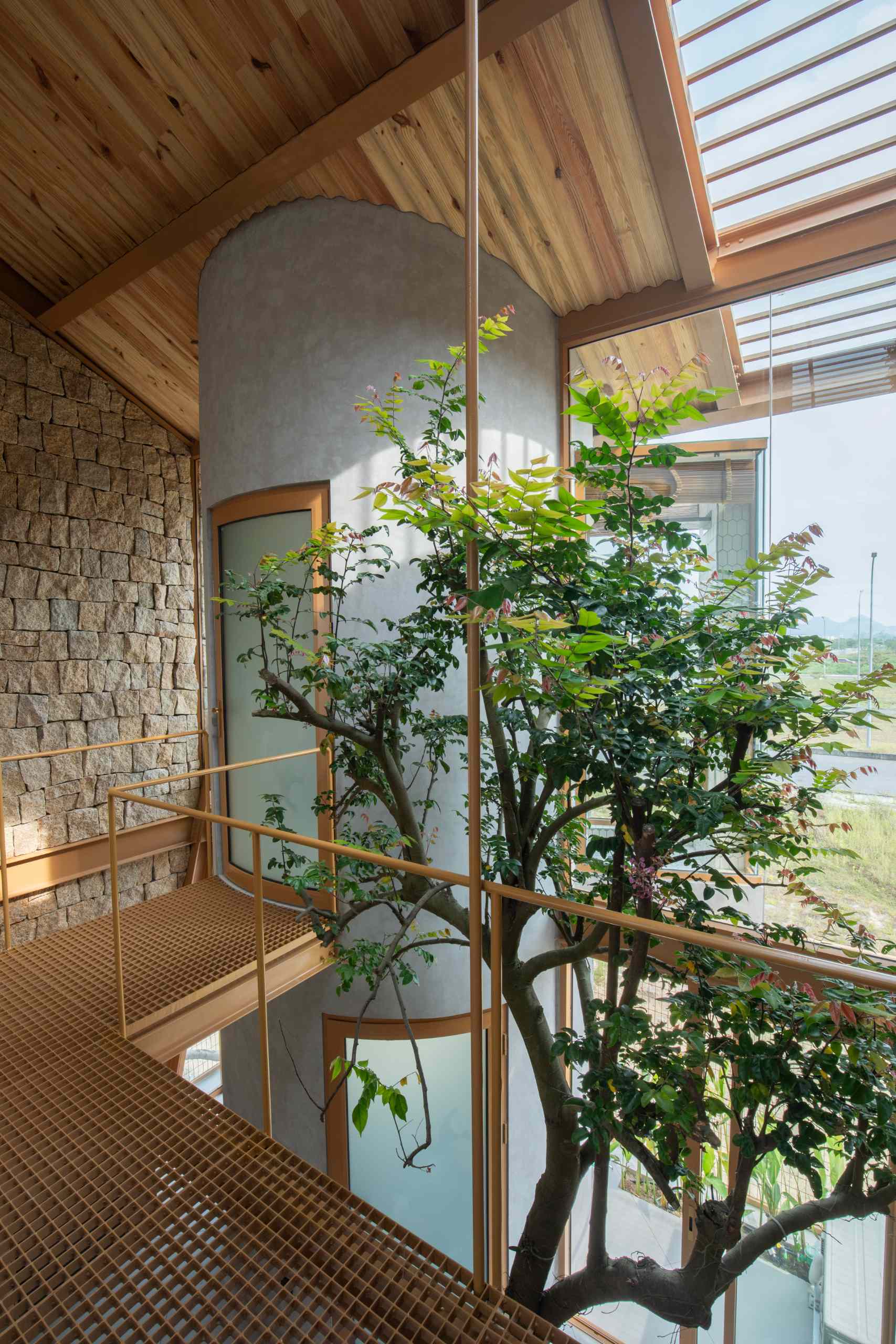 A metal walkway leads to a curved plastered bathroom volume, featuring a frosted glass door with a wood frame. Set between stone and glass walls, it blends raw textures with crisp, modern lines and a floating, elevated feel.