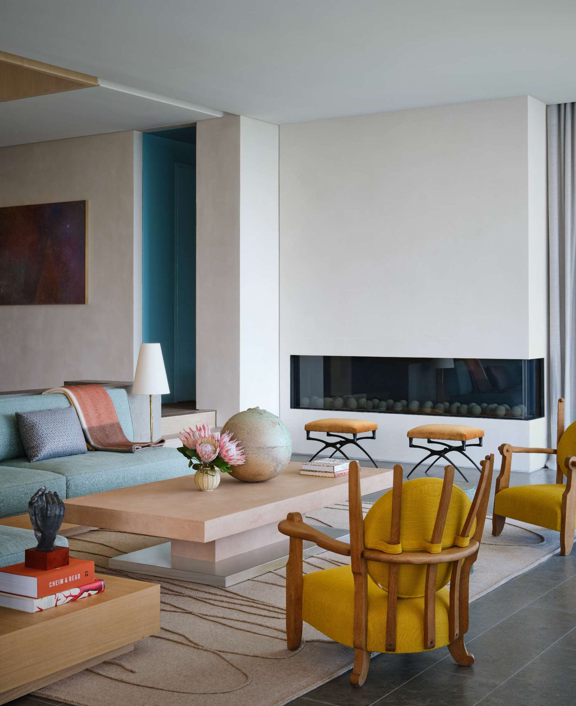 A sleek, horizontal fireplace anchors this living room with minimalist elegance, its dark firebox contrasting the pale wall. Surrounded by sculptural furniture and soft tones, it serves as a refined focal point that blends warmth with modern coastal style.