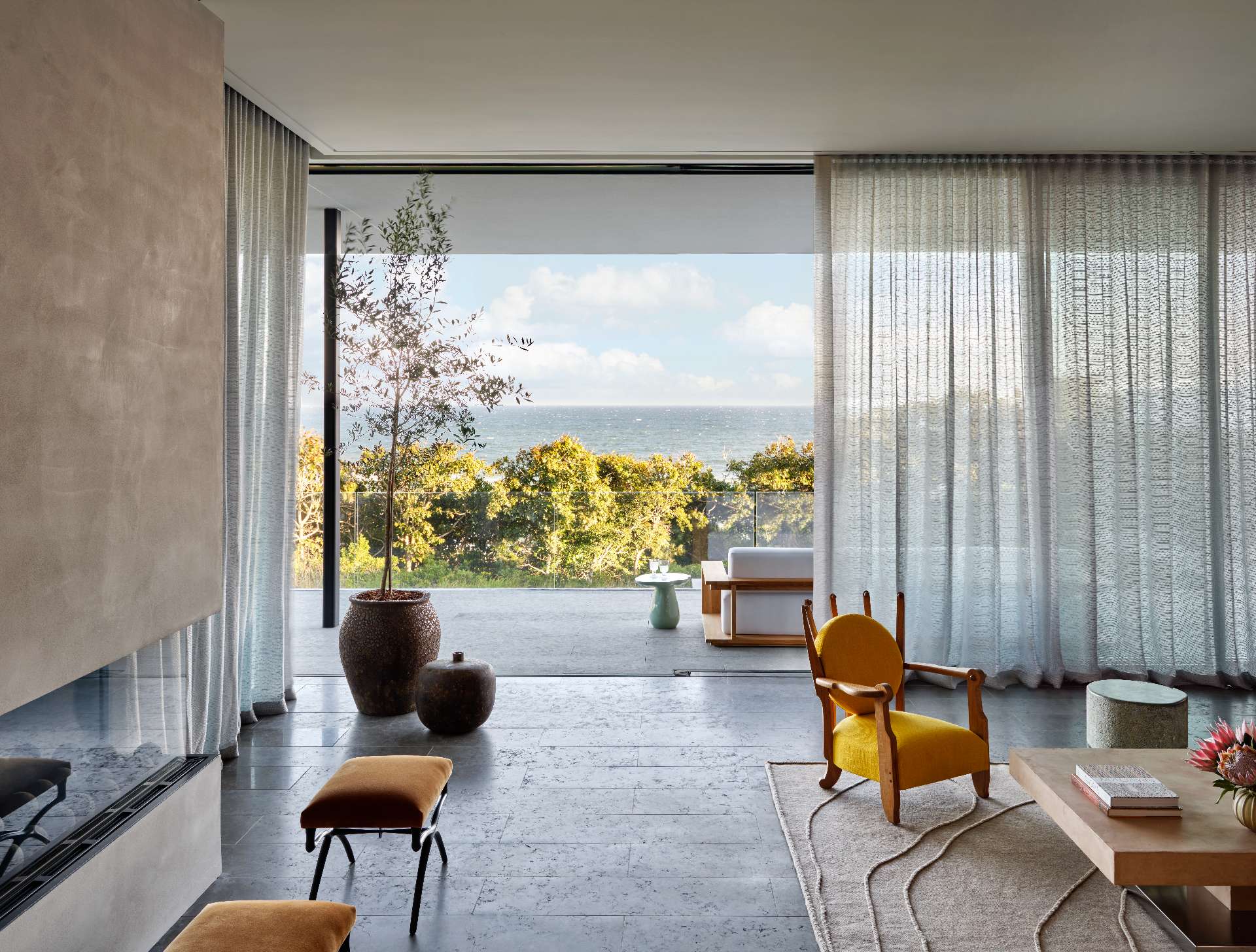A sleek, horizontal fireplace anchors this living room with minimalist elegance, its dark firebox contrasting the pale wall. Surrounded by sculptural furniture and soft tones, it serves as a refined focal point that blends warmth with modern coastal style.