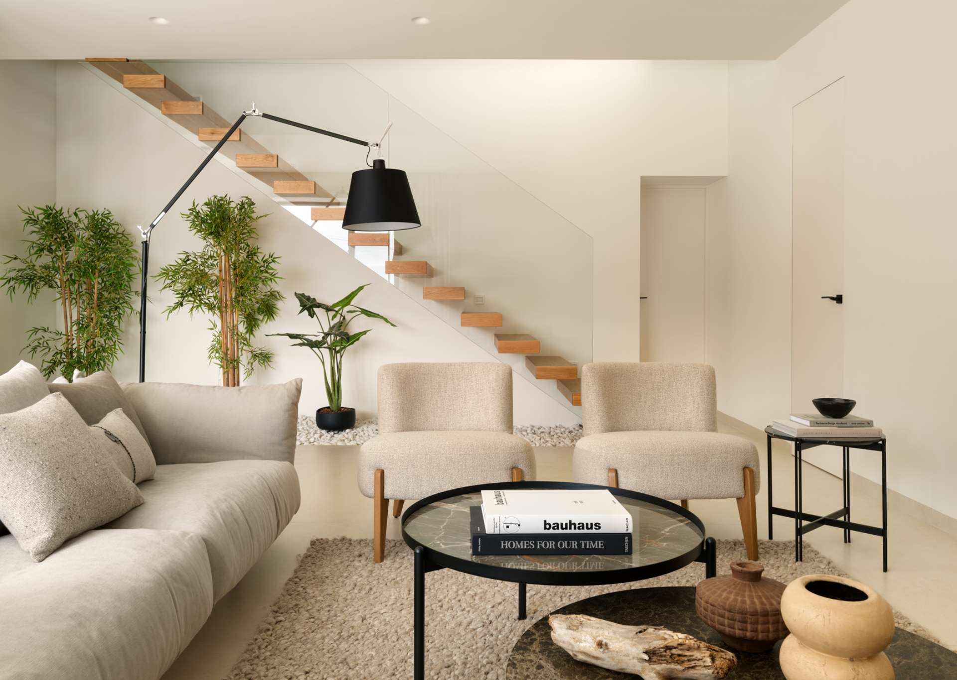 Floating timber stairs by the living room become a sculptural focal point in the home, rising gracefully above a bed of white stones and greenery.