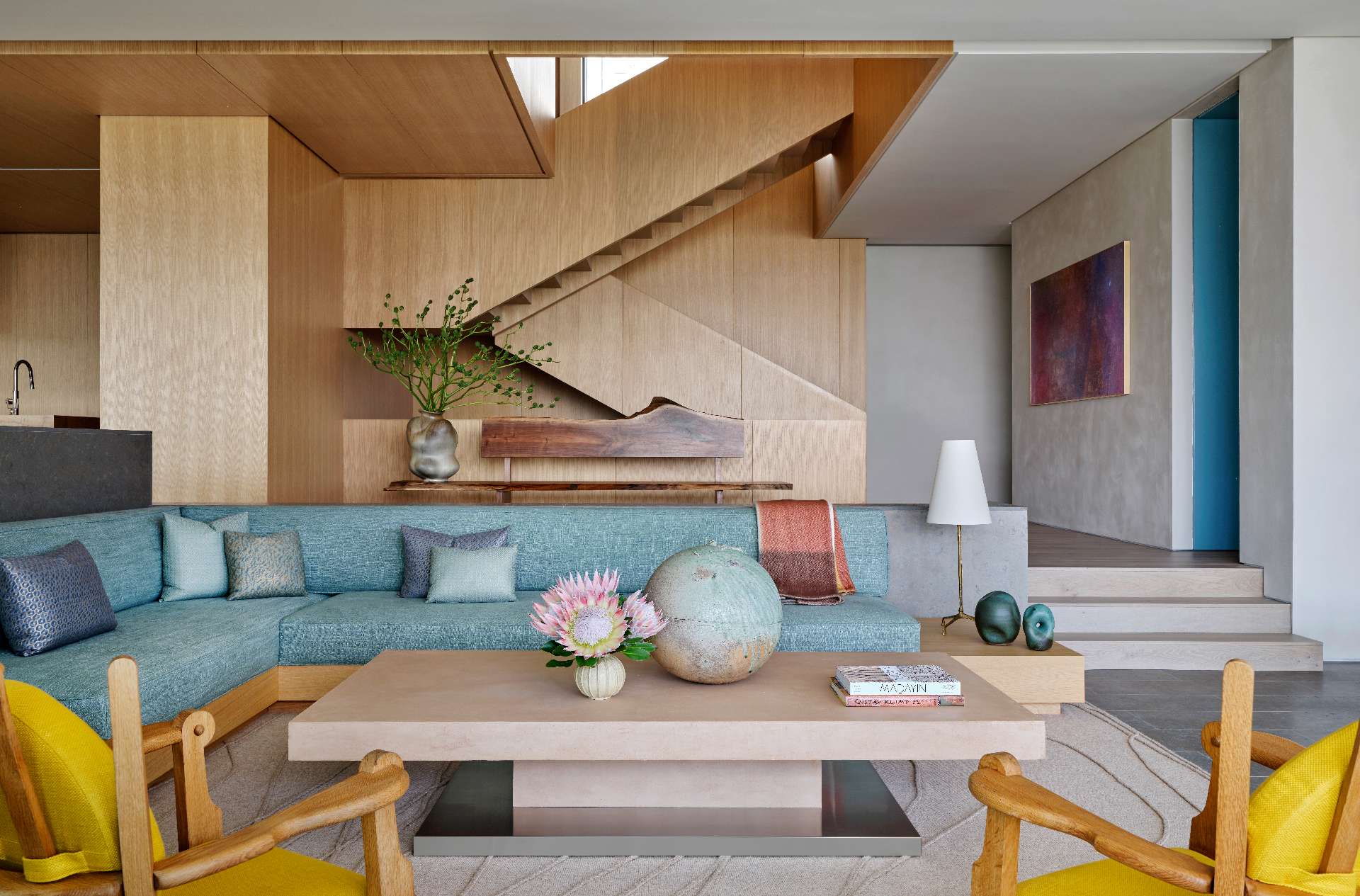 A sunken seating area with soft blue tones creates an intimate gathering space, while artful touches, like a sculptural wooden bench and abstract painting, add character without overwhelming the serene aesthetic.