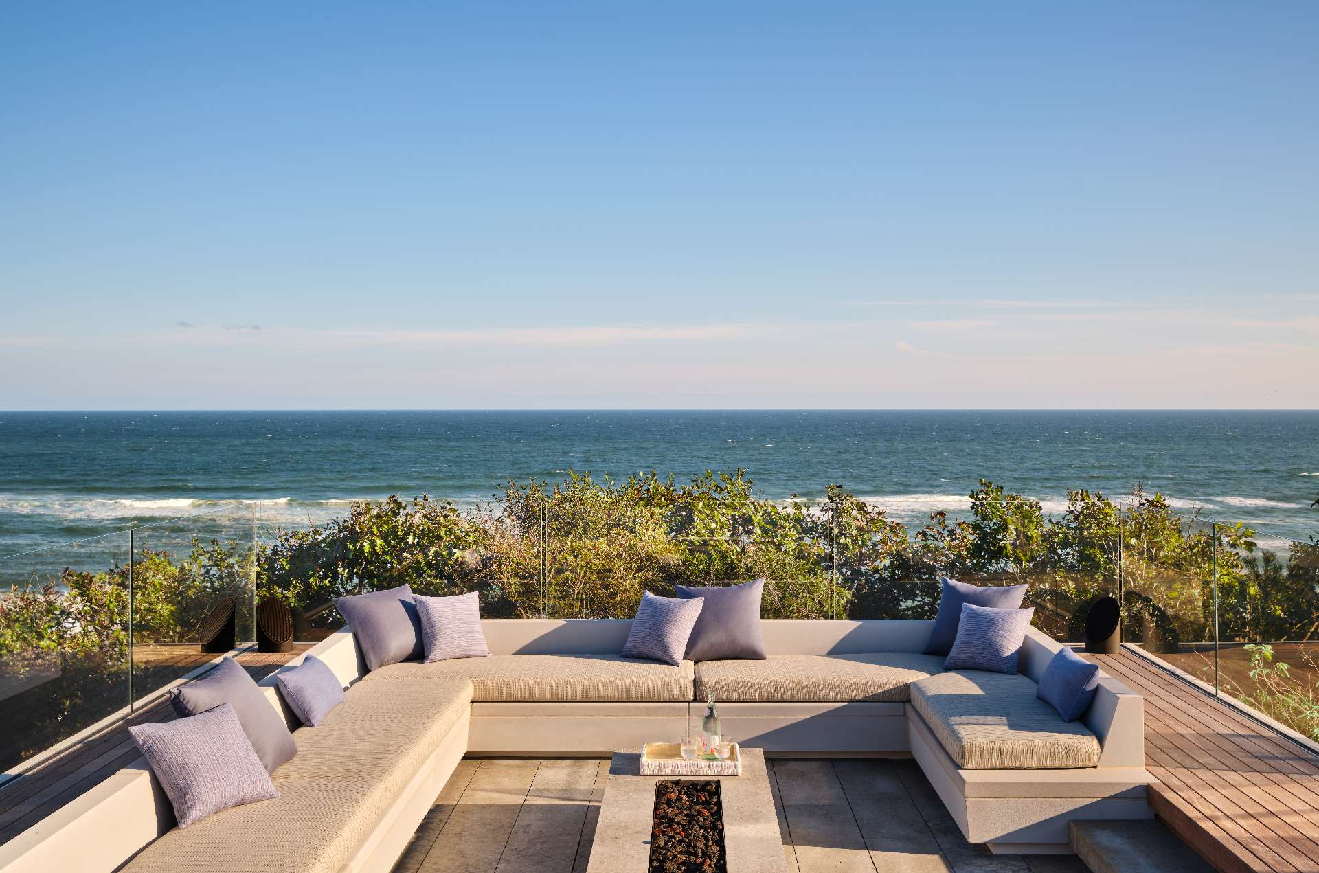 Perched at the edge of the bluff, an intimate firepit lounge offers panoramic water views. Framed by low glass railings, the built-in seating creates a wind-sheltered retreat that blurs the line between comfort and coastline.