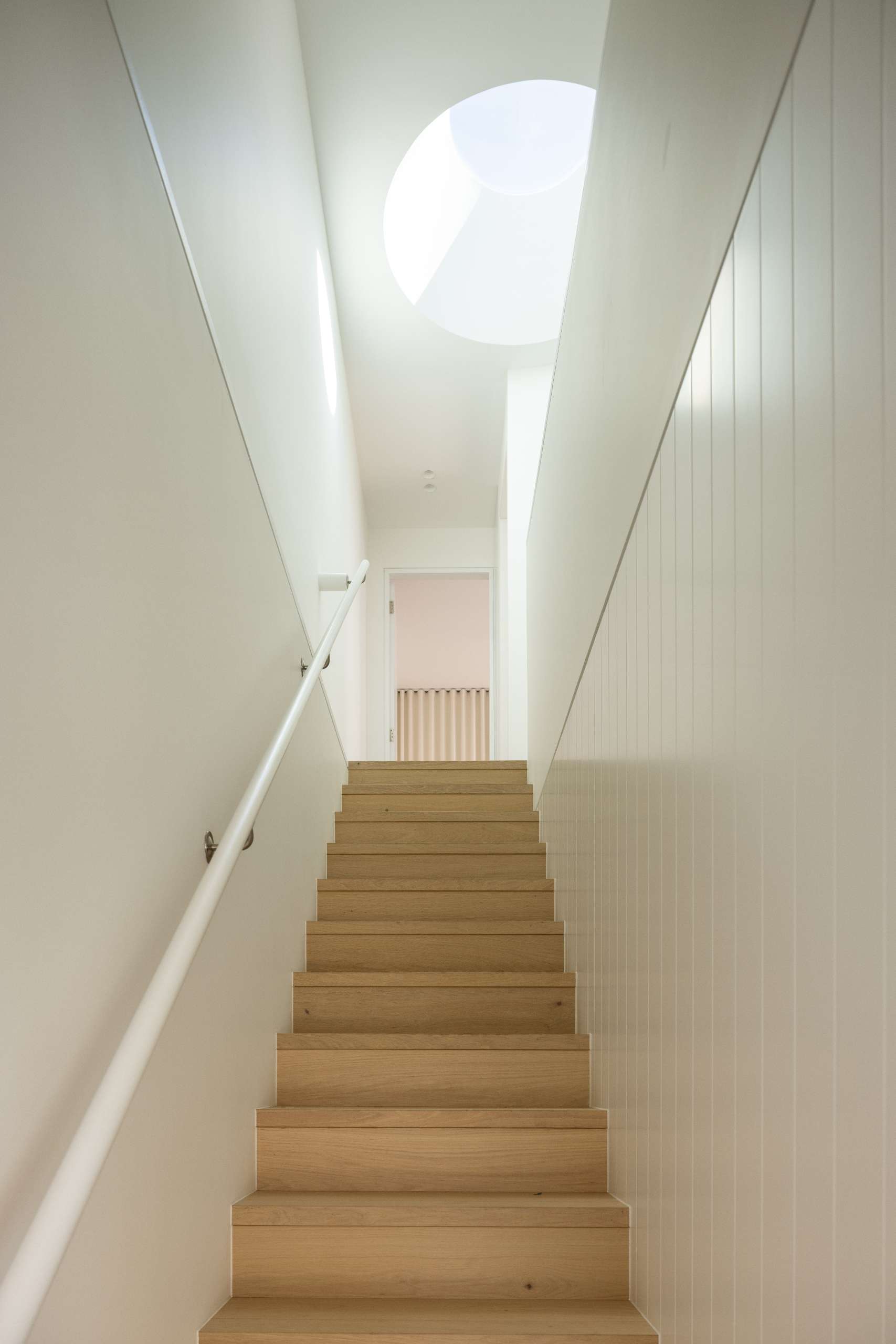This staircase is tucked behind a blade wall near the kitchen, continuing the home's palette of timber, concrete, and white finishes. Its concealed placement maintains clean architectural lines and adds a quiet sense of discovery as you move through the space.