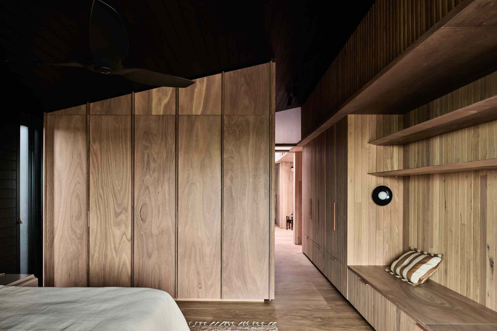 This bedroom is enveloped in warm timber tones, creating a serene, cocoon-like retreat. Custom cabinetry and integrated shelving offer seamless storage, while built-in seating adds comfort and functionality.