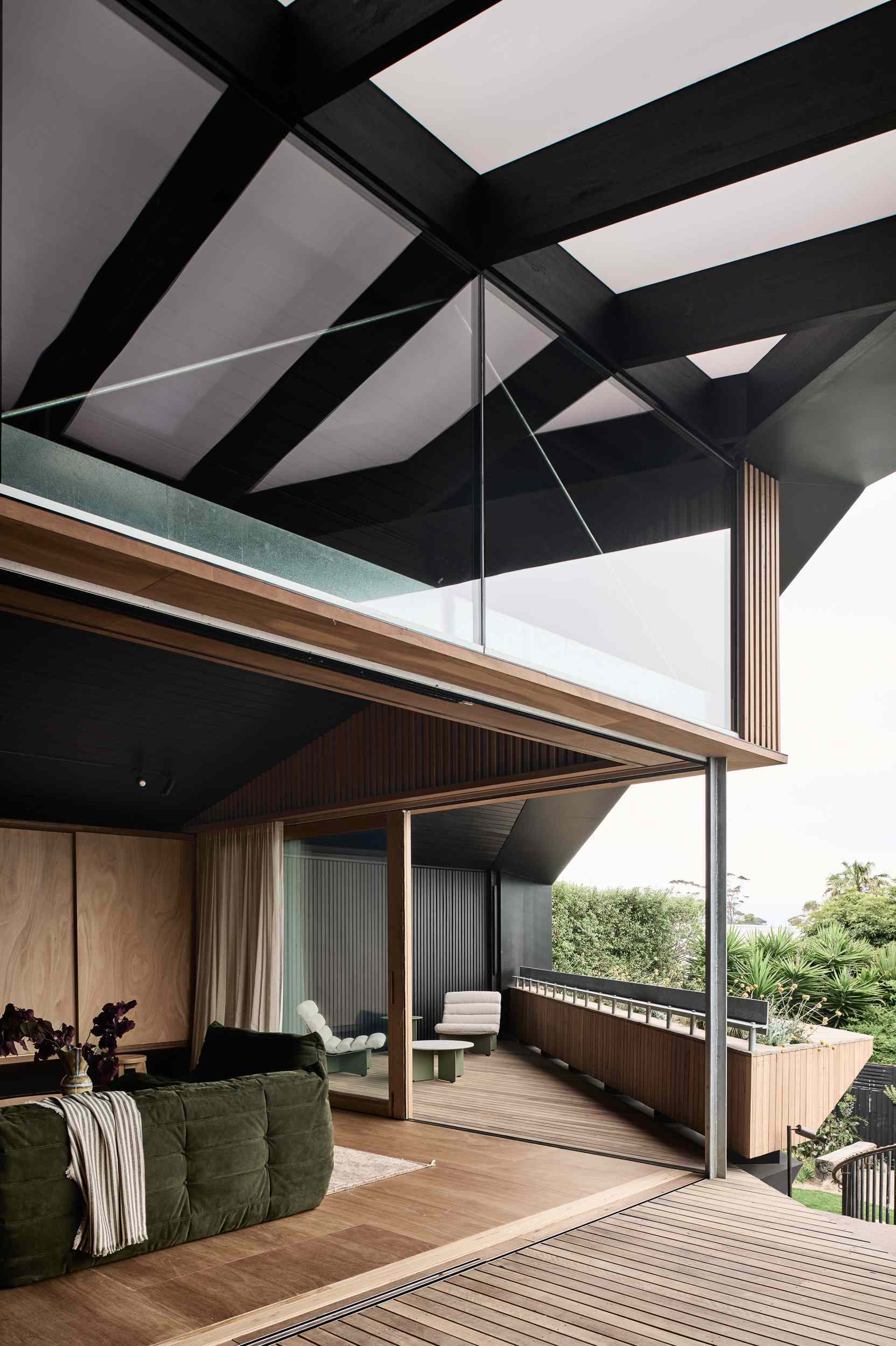 Wood-framed sliding glass walls blur the line between indoors and out, filling the home with natural light and framing peaceful landscape views. When open, they create a seamless flow from the interior to the timber decks and garden beyond.