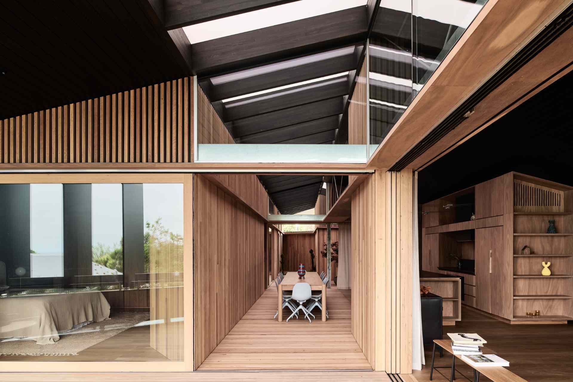 Wood-framed sliding glass walls blur the line between indoors and out, filling the home with natural light and framing peaceful landscape views. When open, they create a seamless flow from the interior to the timber decks and garden beyond.