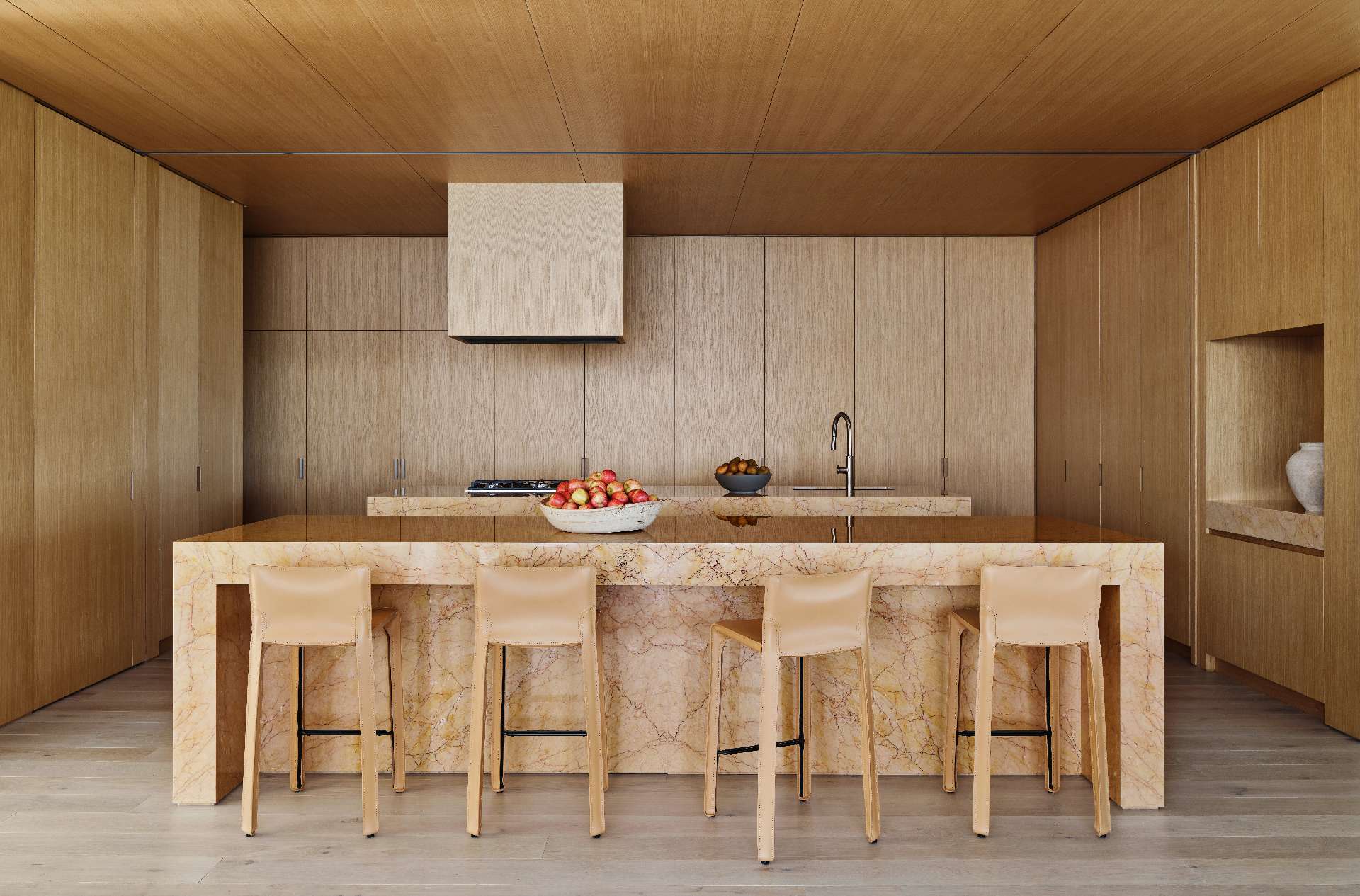 Anchored by a pair of dramatic stone islands, the kitchen strikes a refined balance between natural warmth and sculptural elegance. Wood cabinetry wraps the space seamlessly, concealing appliances and enhancing the minimalist aesthetic.