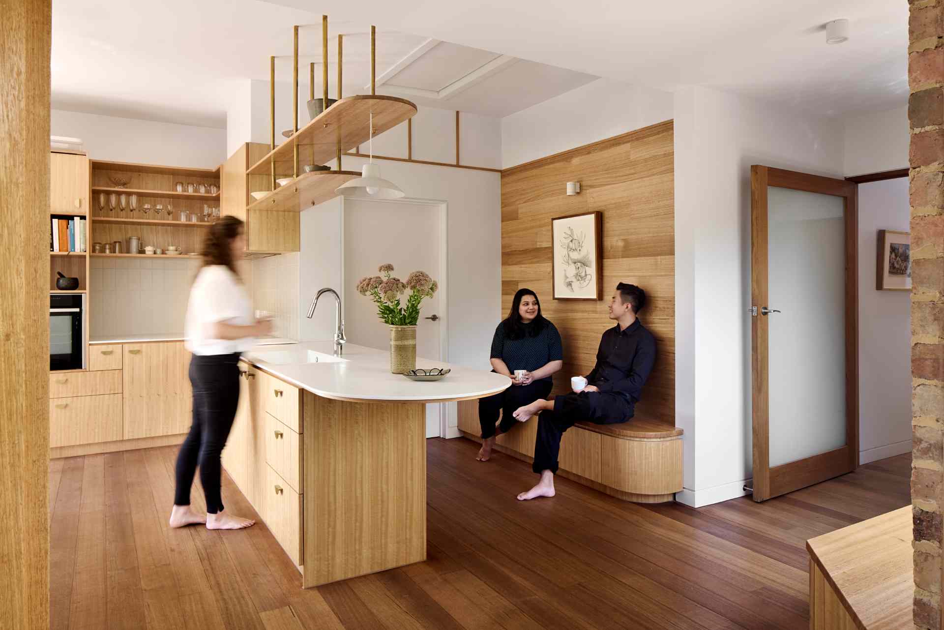 A contemporary kitchen with wood cabinets and white countertops, also includes a variety of seating options in the form of built-in benches.