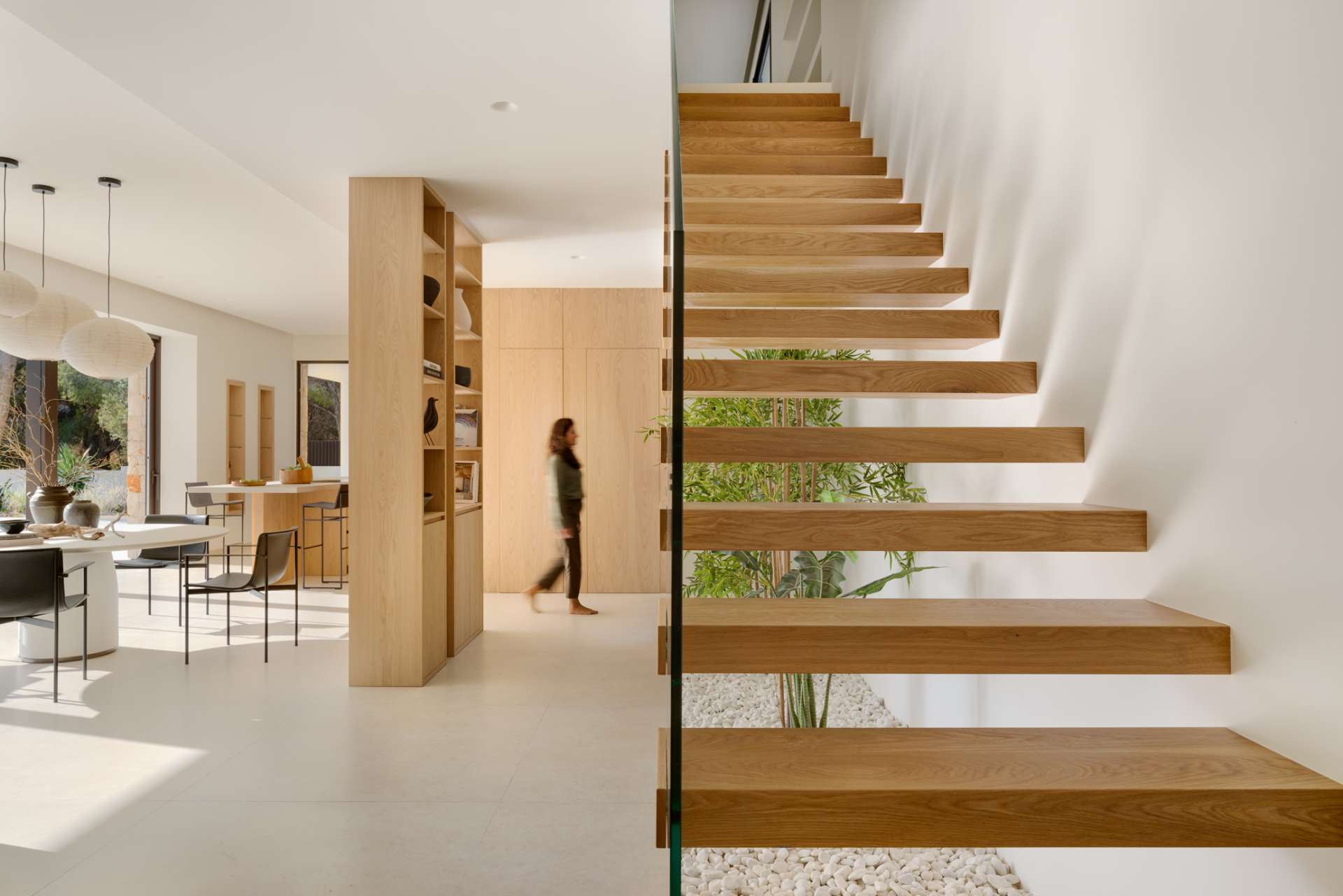 Floating timber stairs by the living room become a sculptural focal point in the home, rising gracefully above a bed of white stones and greenery.