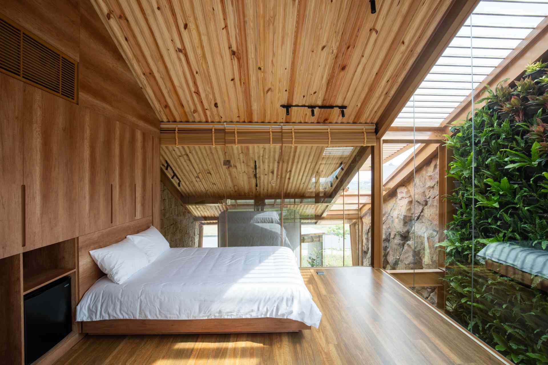 Bedroom with a pitched wooden ceiling, custom built-in cabinetry, and beds positioned between two walls of floor-to-ceiling glass that flood the space with natural light.