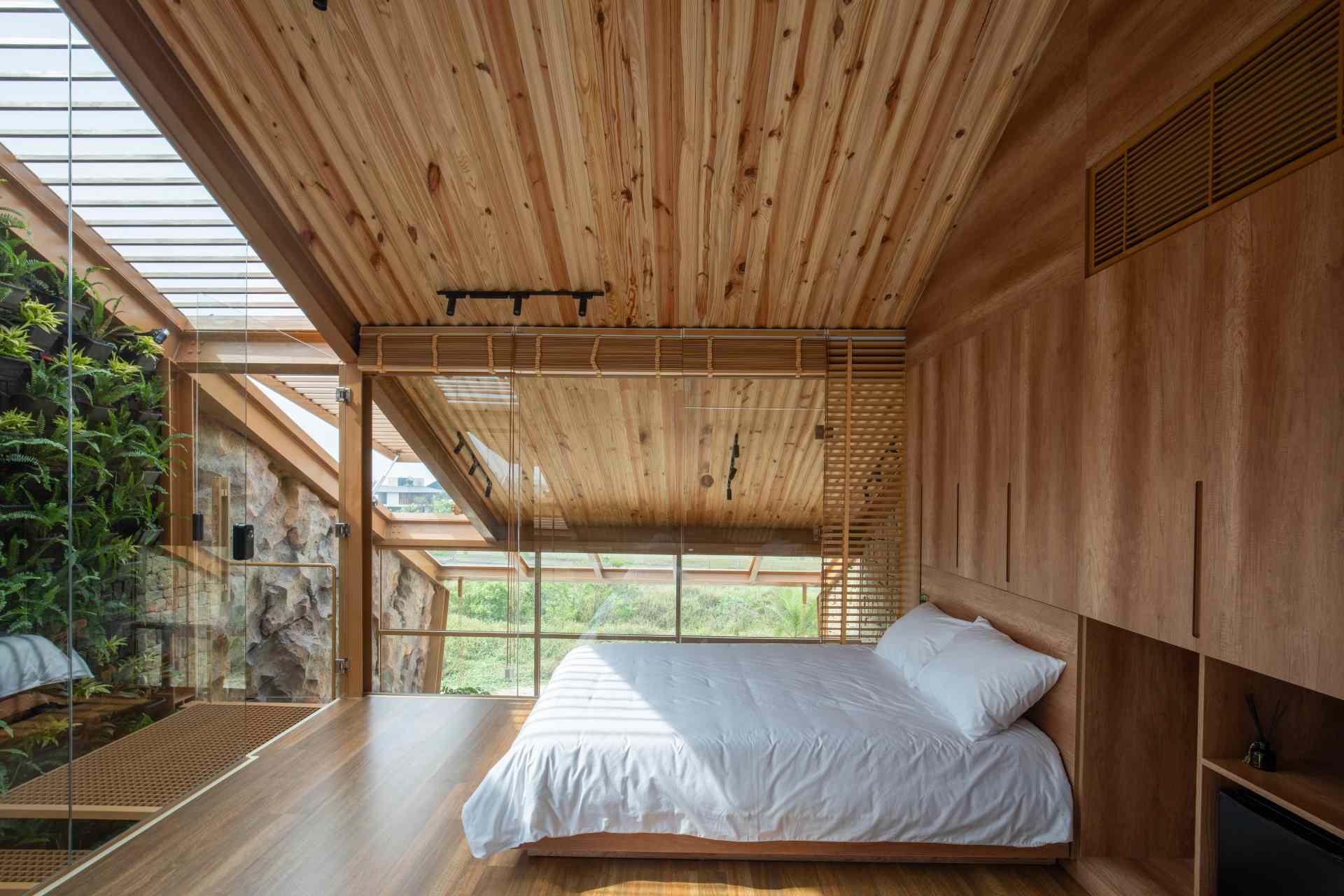 Bedroom with a pitched wooden ceiling, custom built-in cabinetry, and beds positioned between two walls of floor-to-ceiling glass that flood the space with natural light.