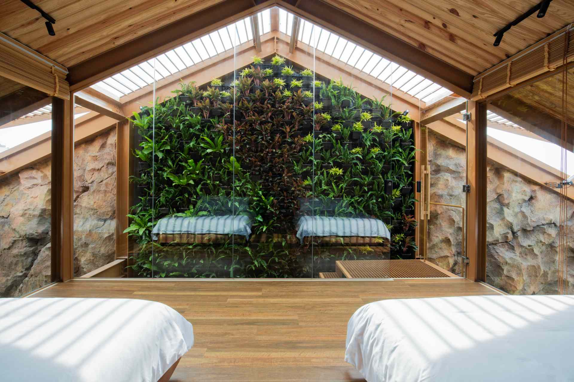 Bedroom with a pitched wooden ceiling, custom built-in cabinetry, and beds positioned between two walls of floor-to-ceiling glass that flood the space with natural light.